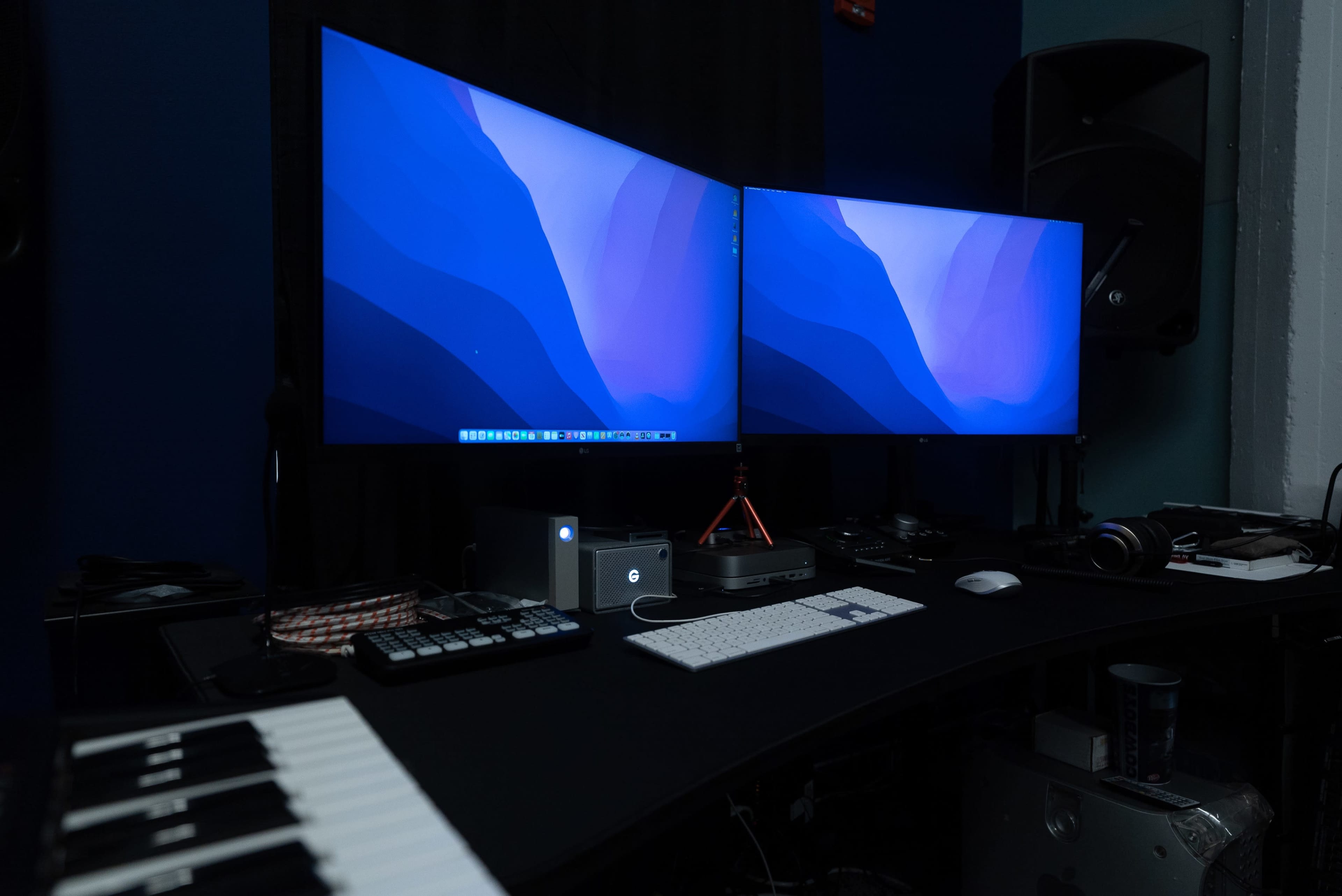 A workstation features two curved monitors, a keyboard, and various electronic devices on a black desk.