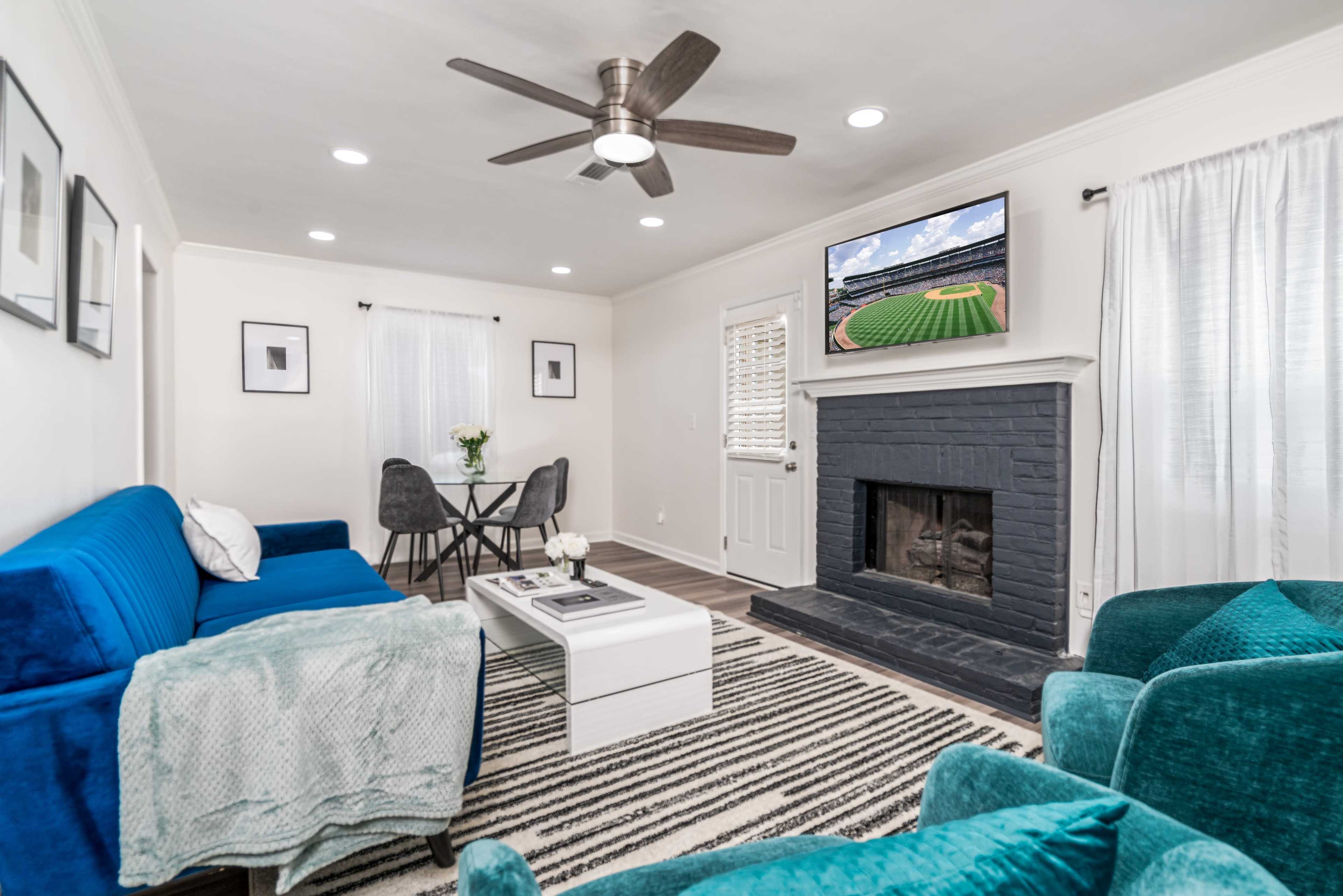 The living room features blue sofas and chairs, a black fireplace, a TV mounted above it, and a small dining area with a round table.
