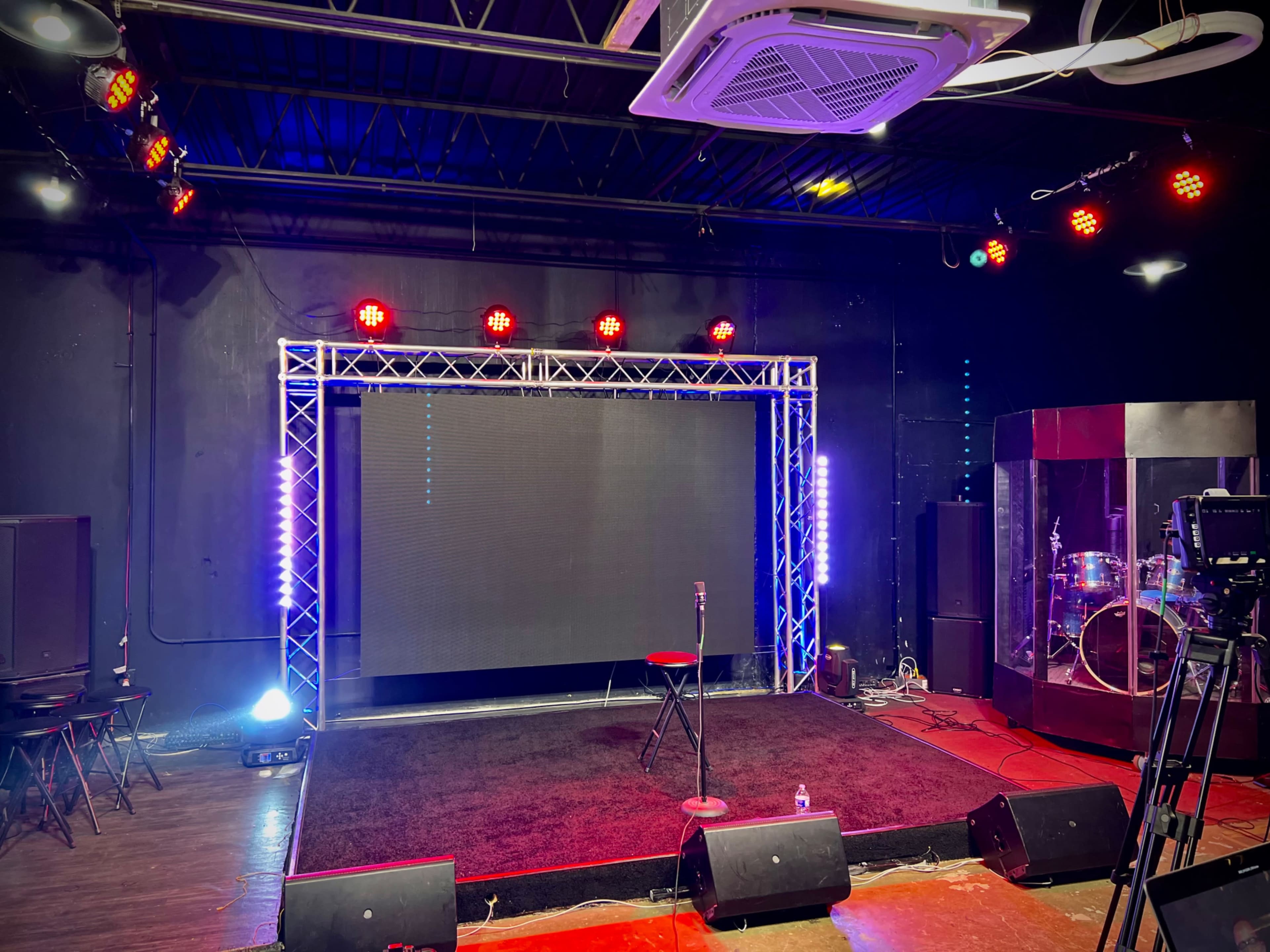 A performance stage with a black background, a red stool, spotlights, and sound equipment set up for a show.
