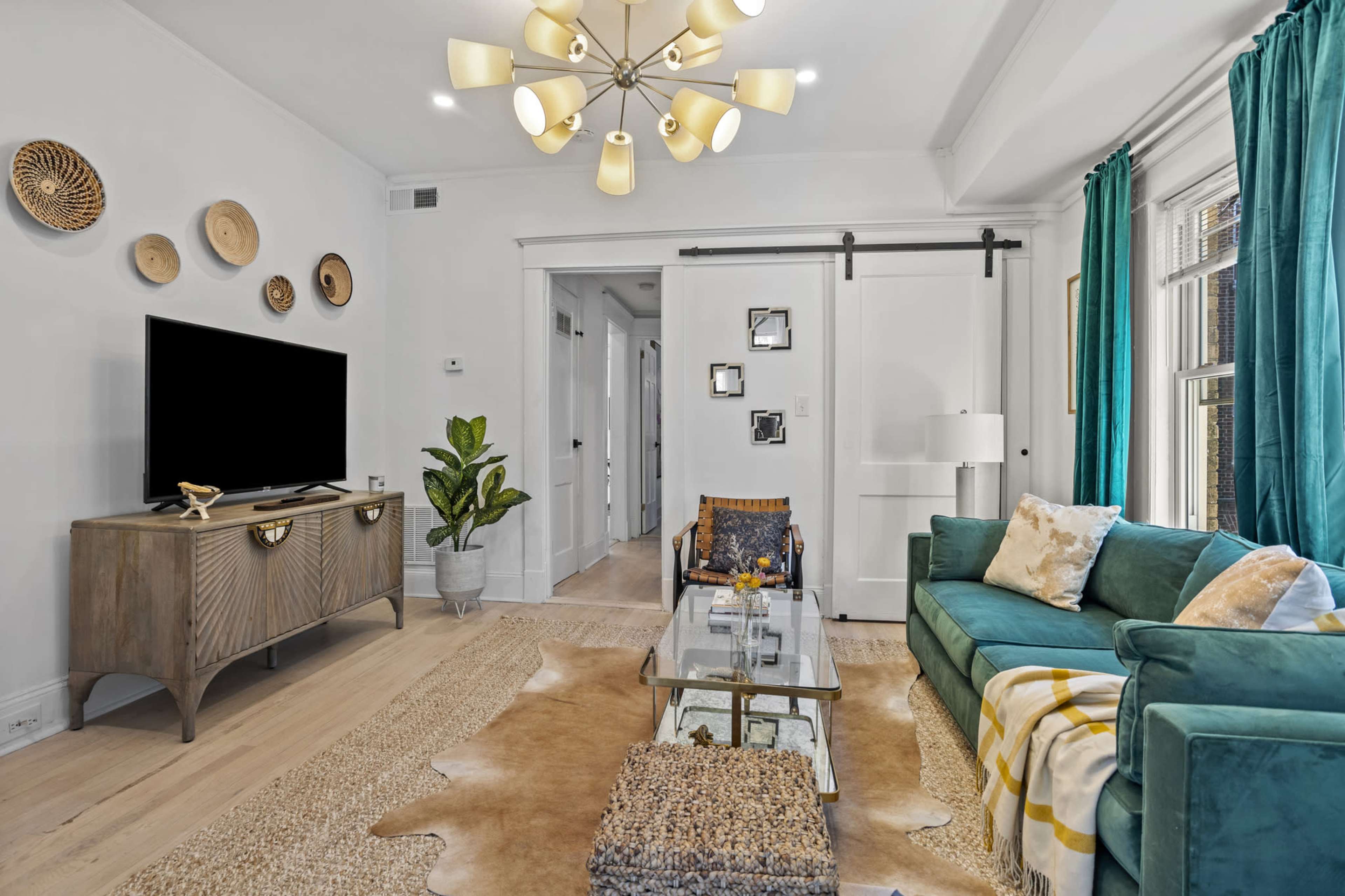 A modern living room with a teal sofa, glass coffee table, and decorative wall plates, accompanied by a flat-screen TV and indoor plant.