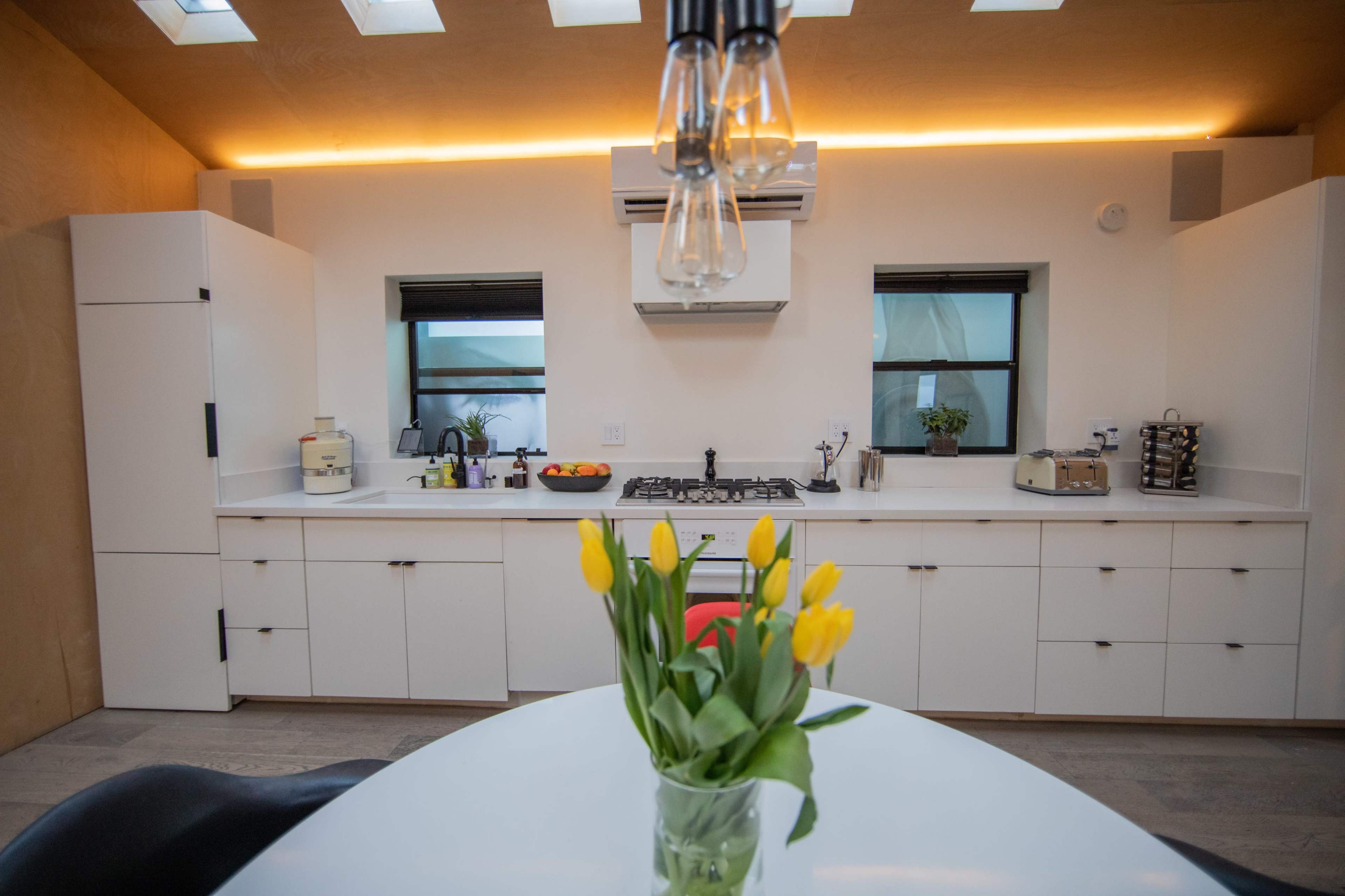 A modern kitchen features white cabinetry, a gas stove, and a round table with a vase of yellow tulips.