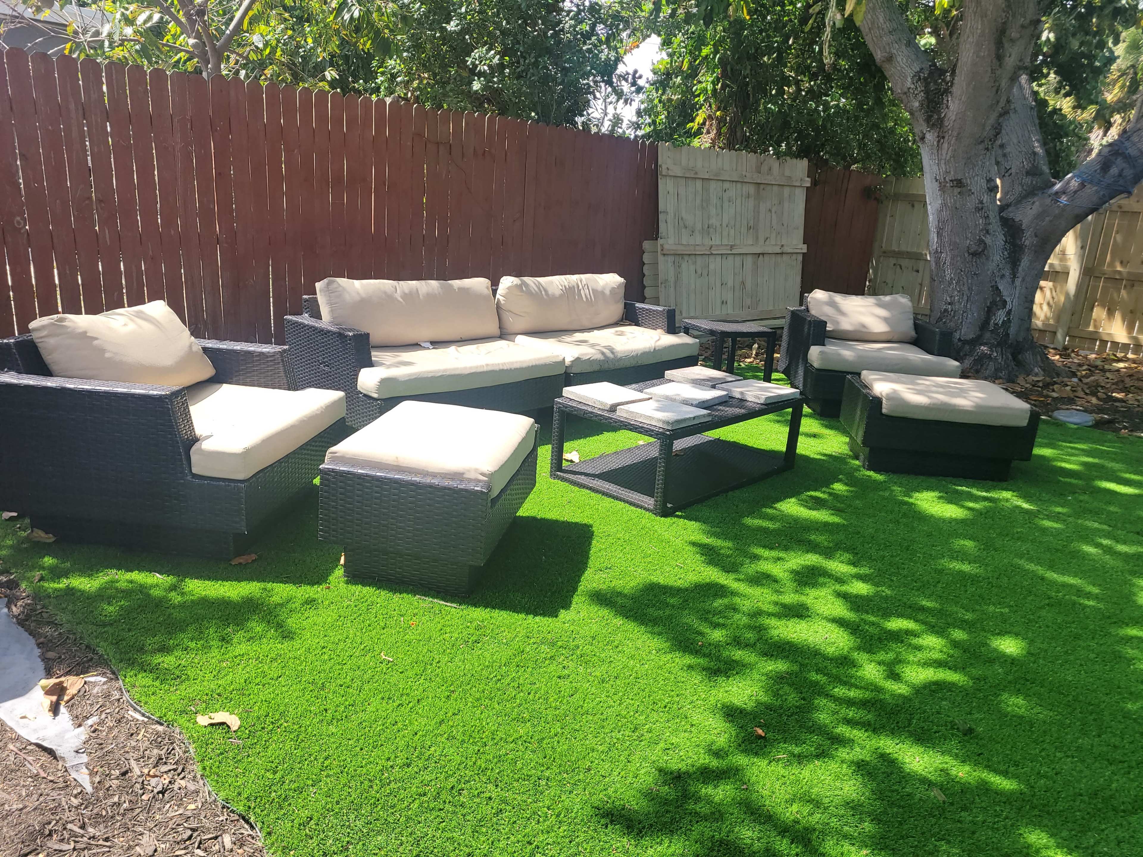 A patio area features a seating arrangement with black wicker furniture and a glass-top table on artificial grass.