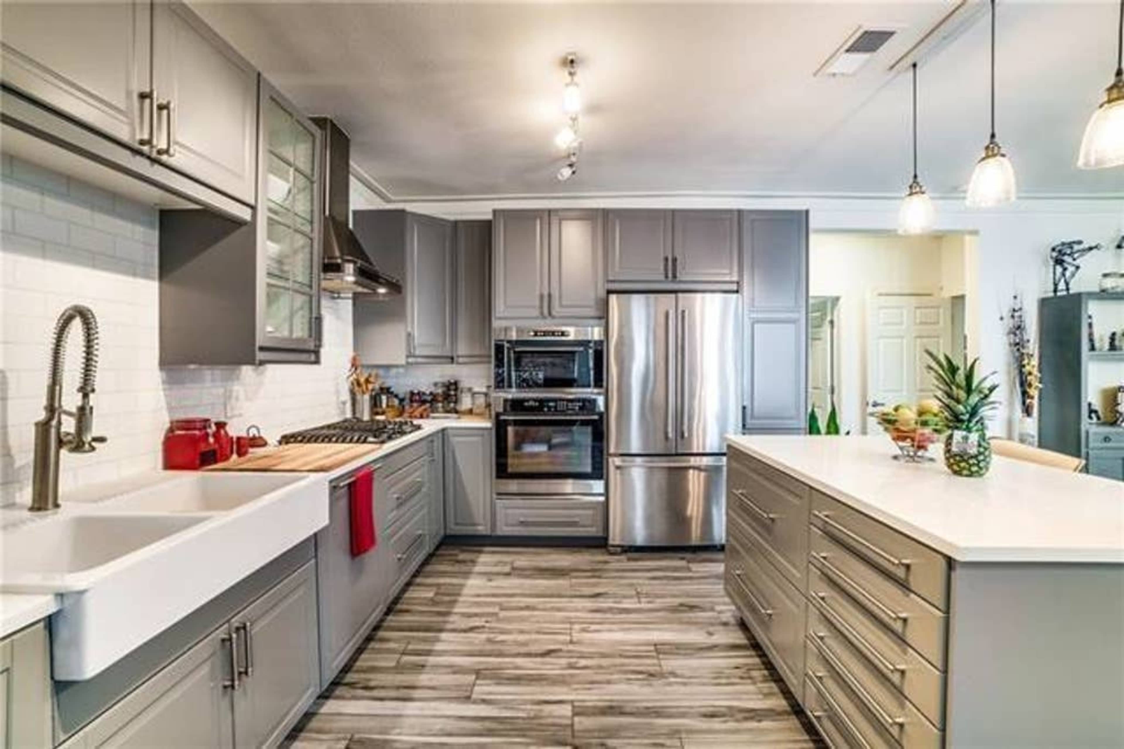 A modern kitchen featuring gray cabinets, stainless steel appliances, and a large central island with a white countertop.