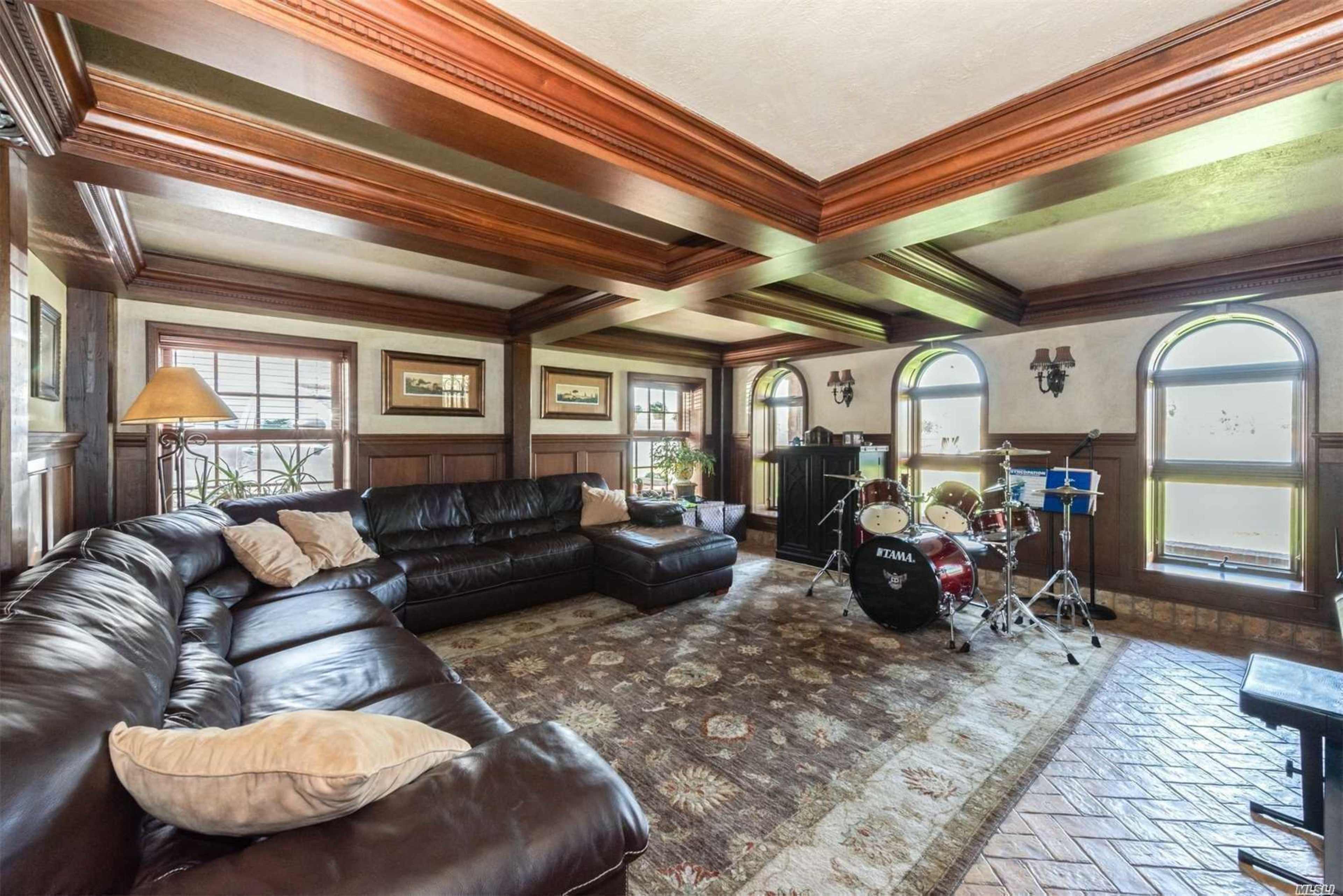 A spacious living room featuring a dark leather sectional sofa, a decorative rug, and a drum set near arched windows.