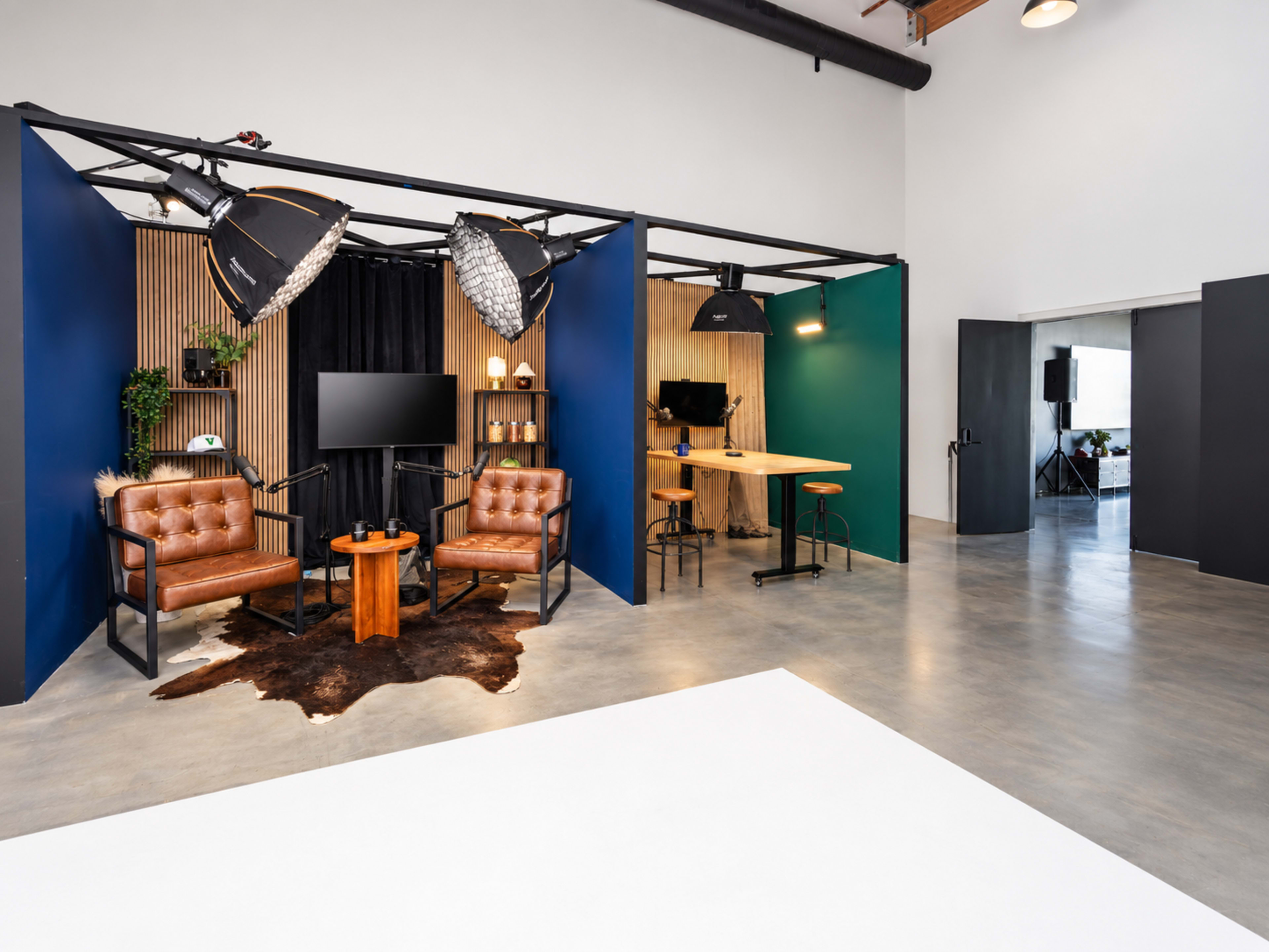 The image features a modern studio space with two leather chairs, a coffee table, and various lighting setups against a backdrop of colorful walls and wood accents.