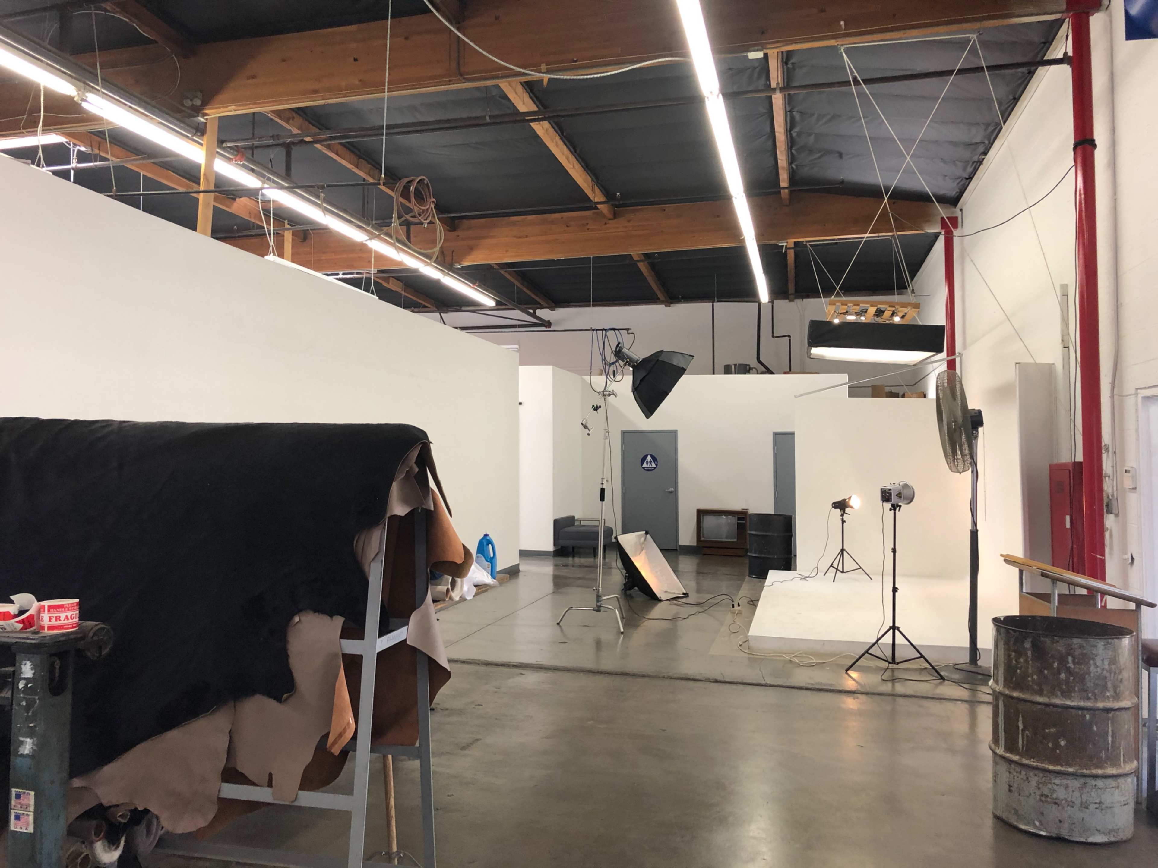 An industrial studio space with a green wall, a backdrop setup, photography equipment, and leather scraps on tables.