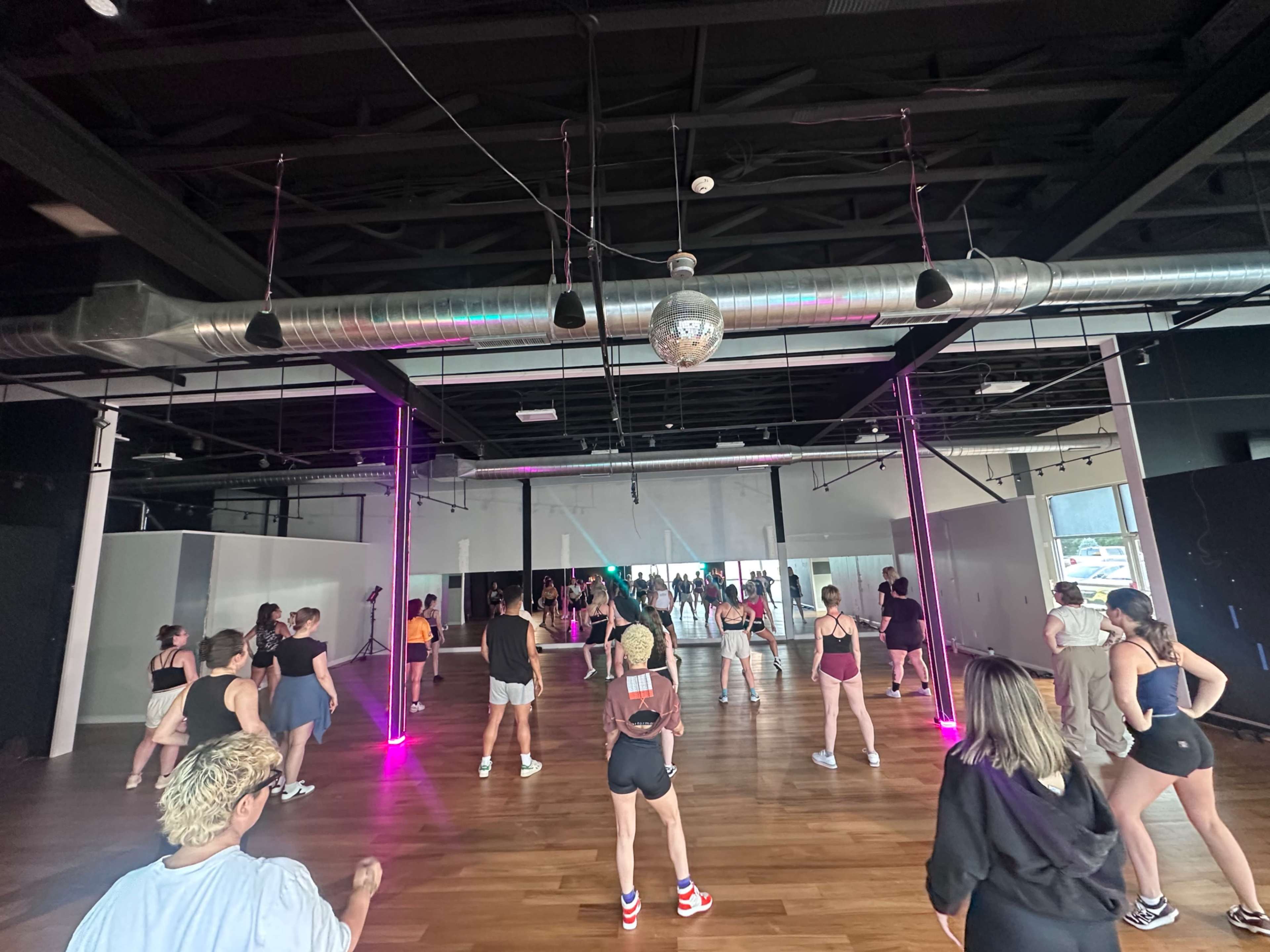 A group of people is participating in a dance class in a studio with wooden floors and vibrant lighting.