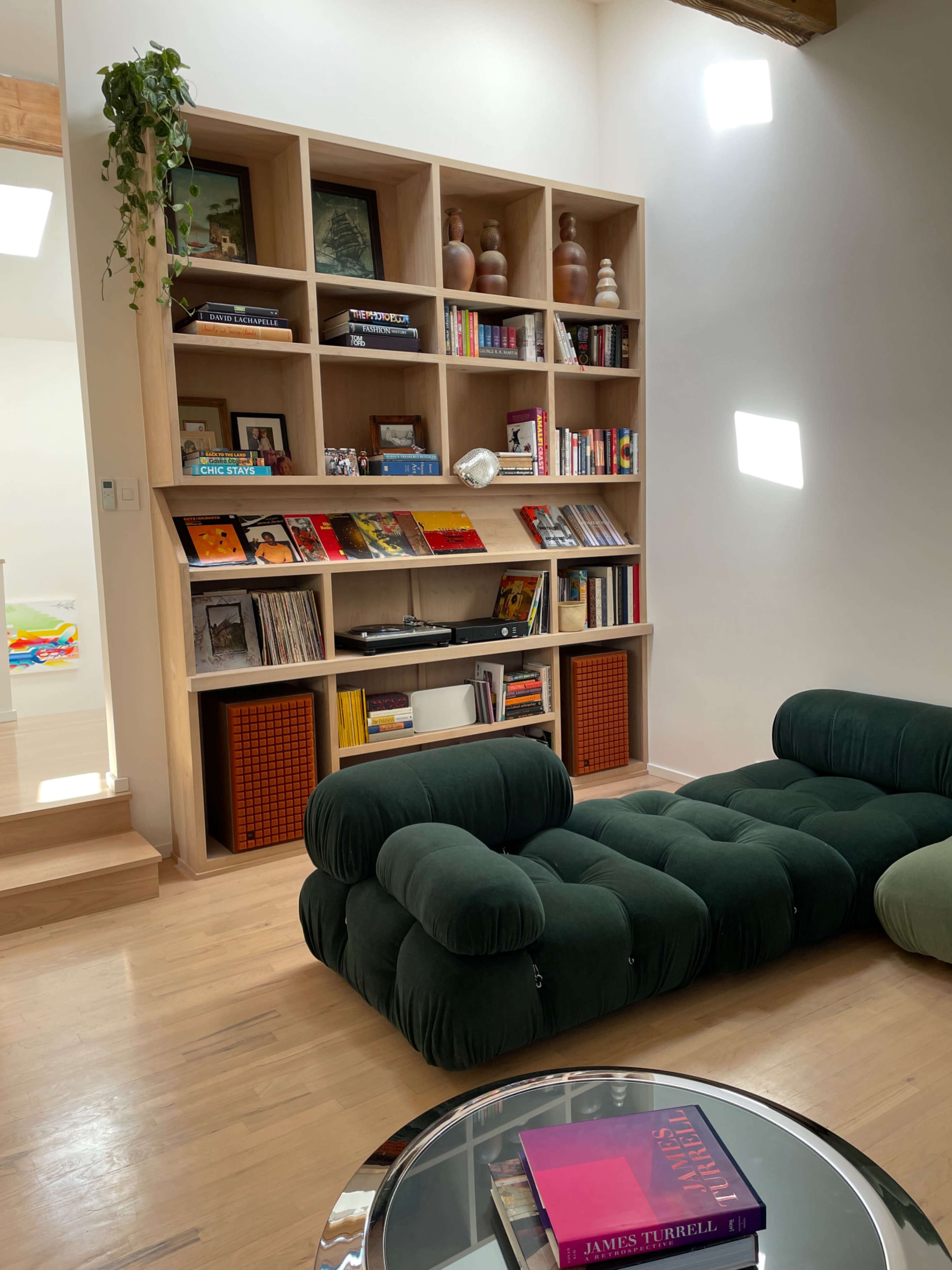A living space with a wooden bookshelf filled with books and decorative items, a round glass coffee table, and a green modular sofa.