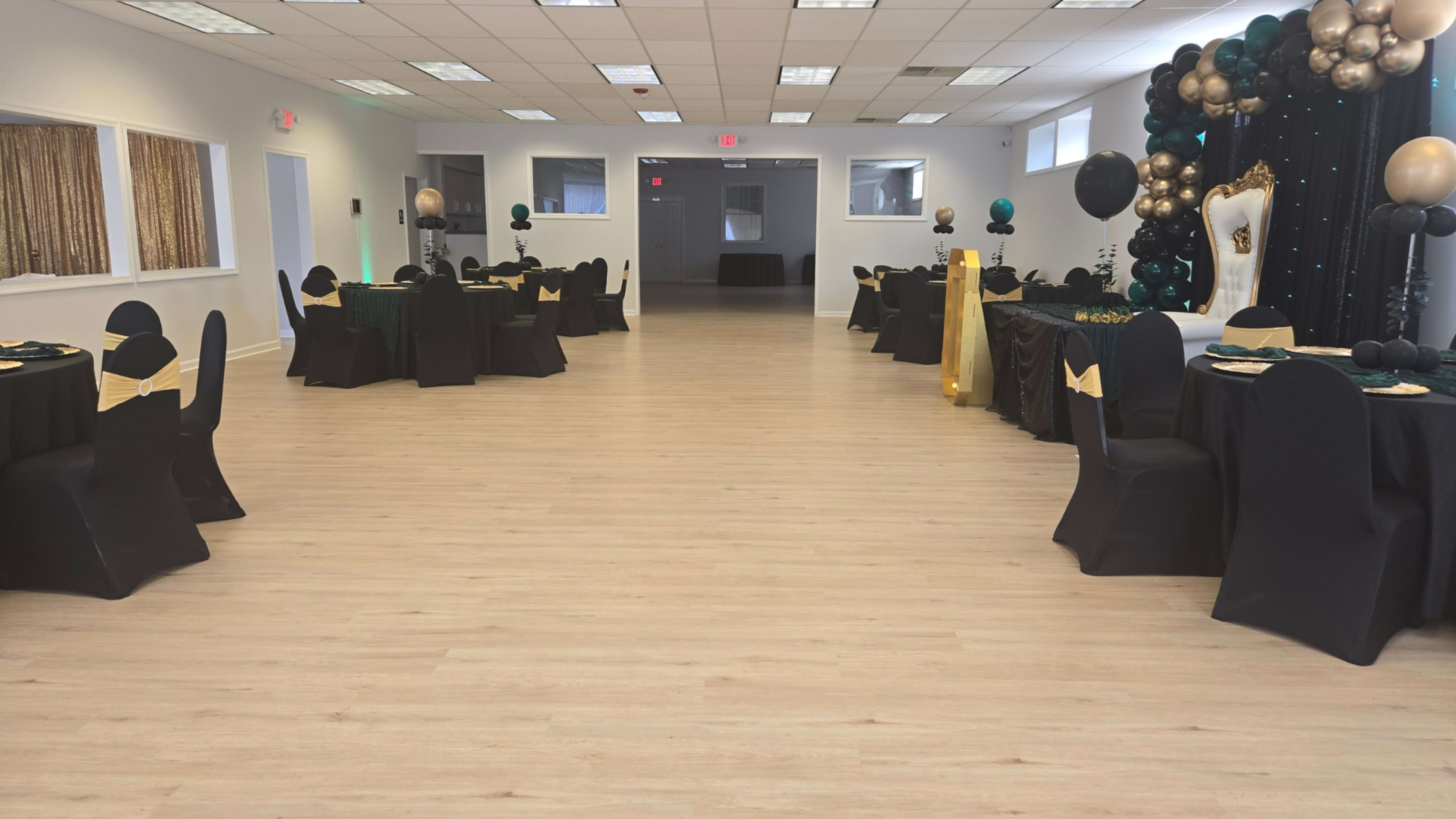 The image shows a banquet hall set up for an event, featuring tables covered in black tablecloths and decorated with green and gold accents.
