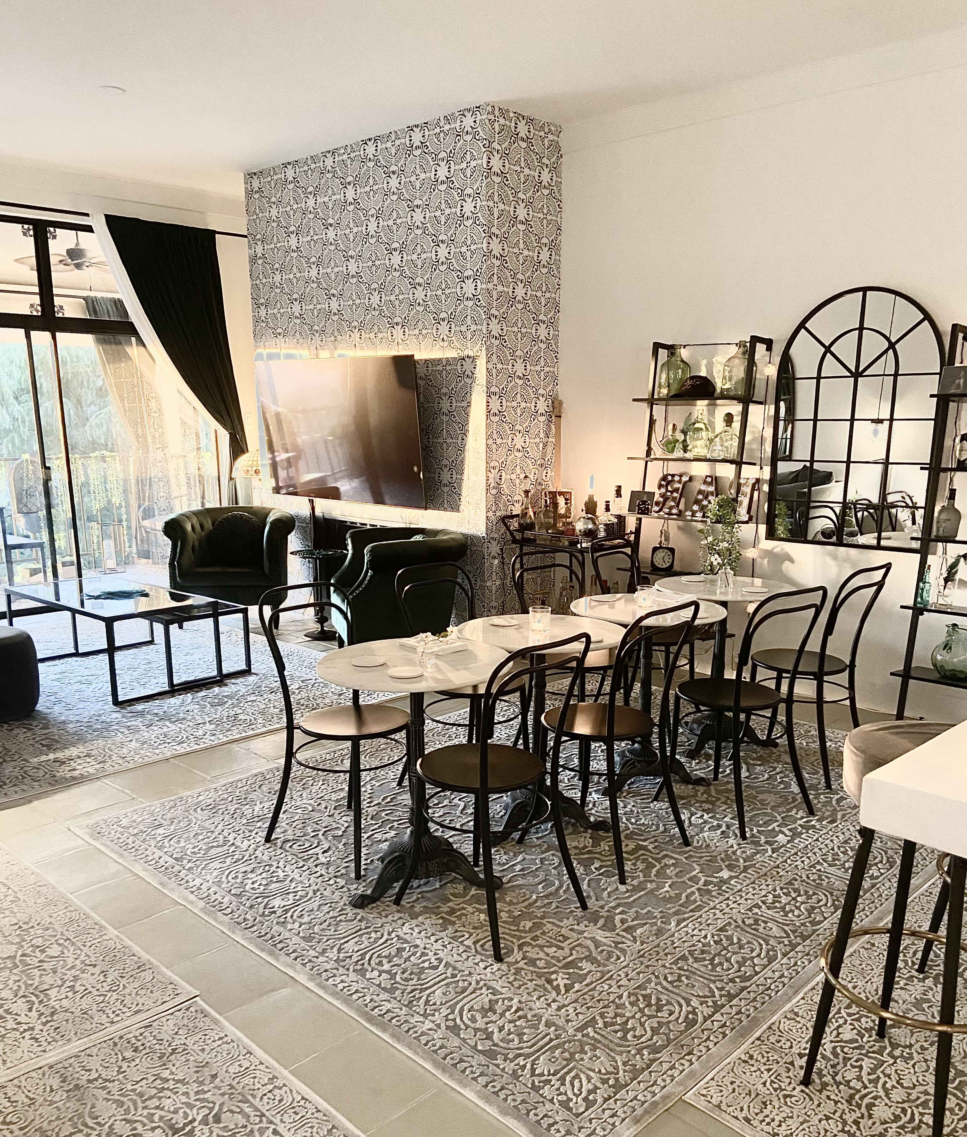 A modern living and dining area featuring a glass dining table surrounded by black and white chairs, a green velvet sofa, and decorative elements on the shelves and walls.