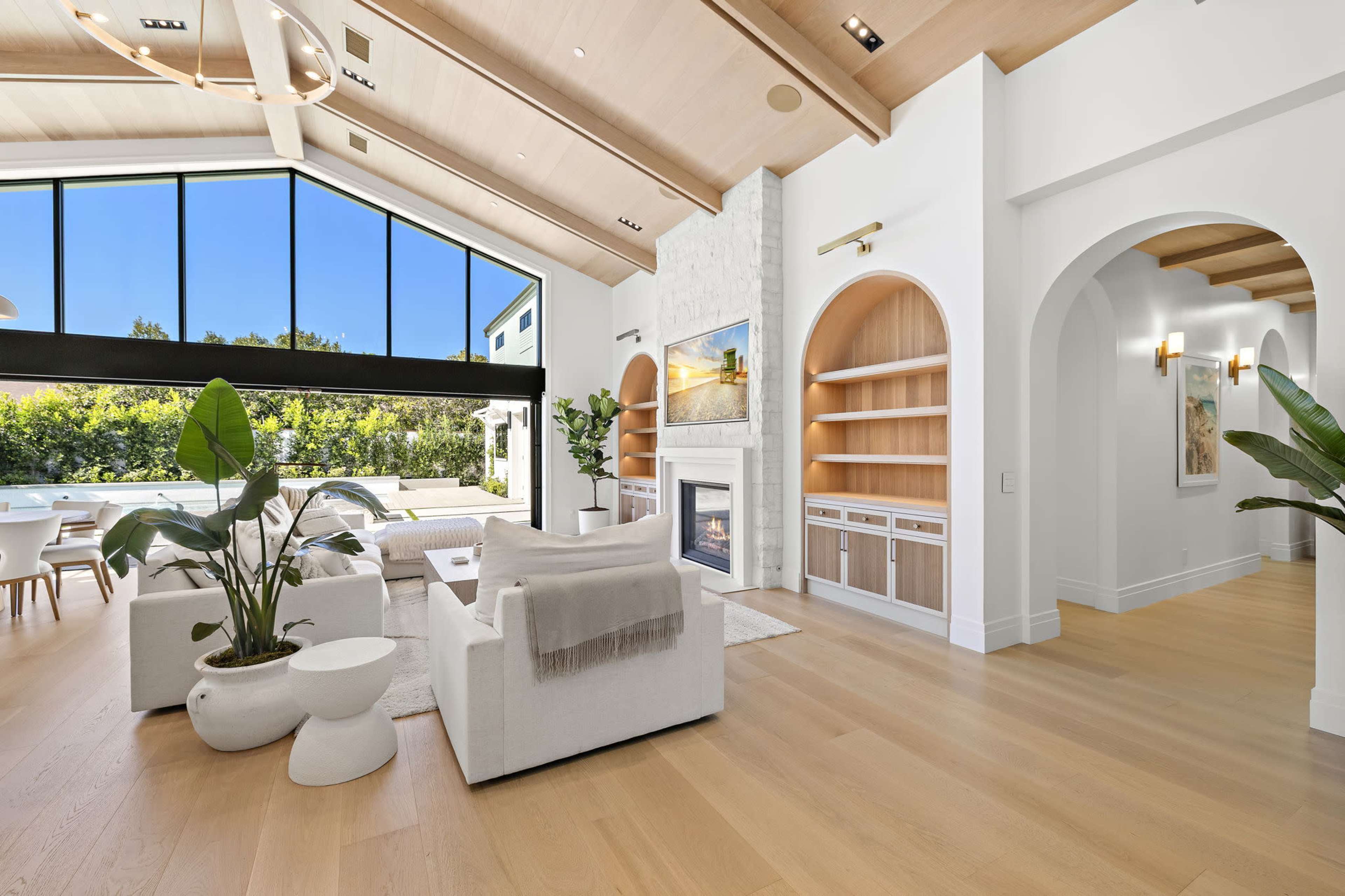 The image shows a spacious, modern living room with large windows, neutral-colored furniture, and a fireplace, enhancing the bright and airy atmosphere.