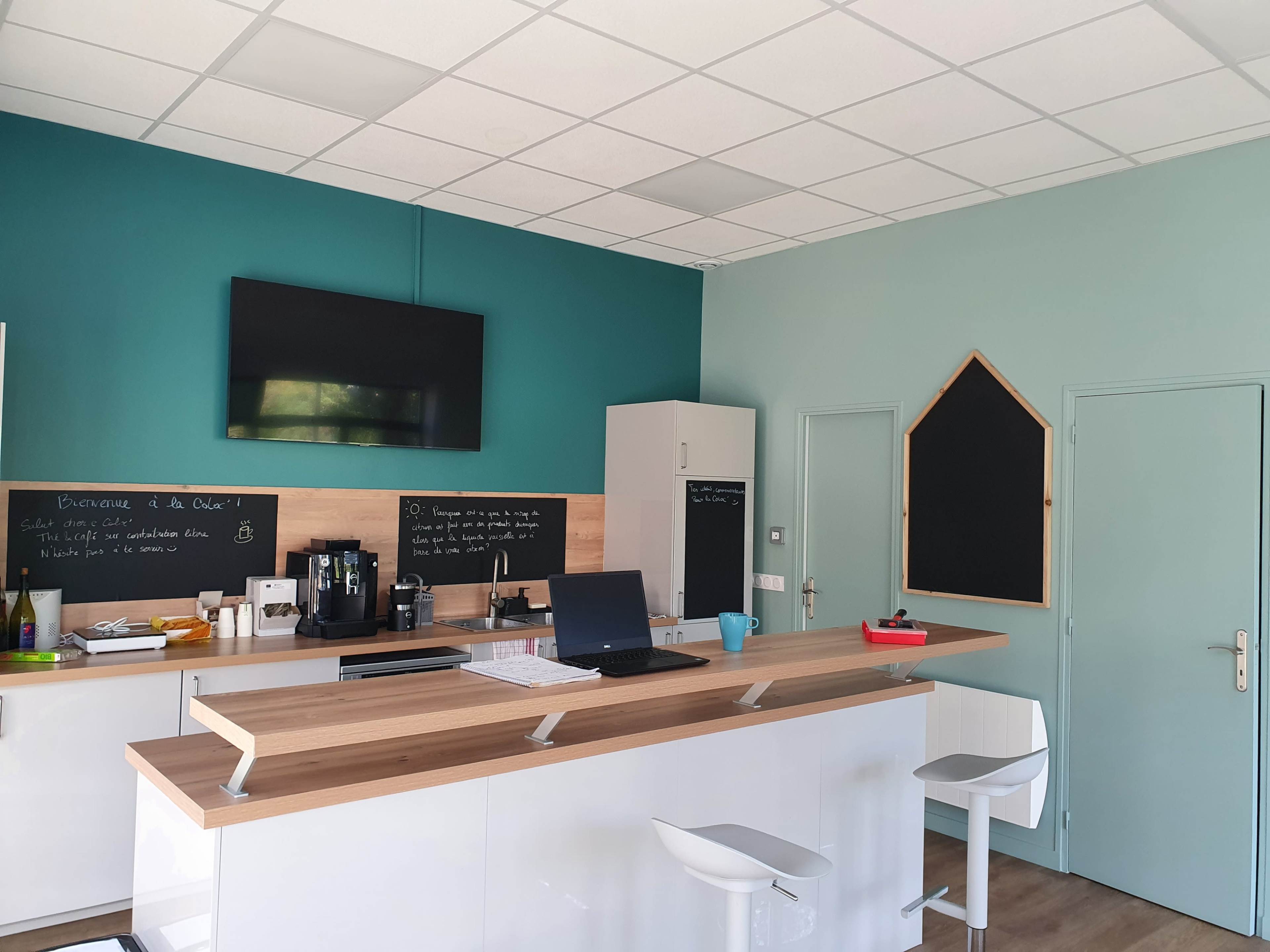 A modern kitchen space with a bar-style counter, a television mounted on the wall, and chalkboards for notes.