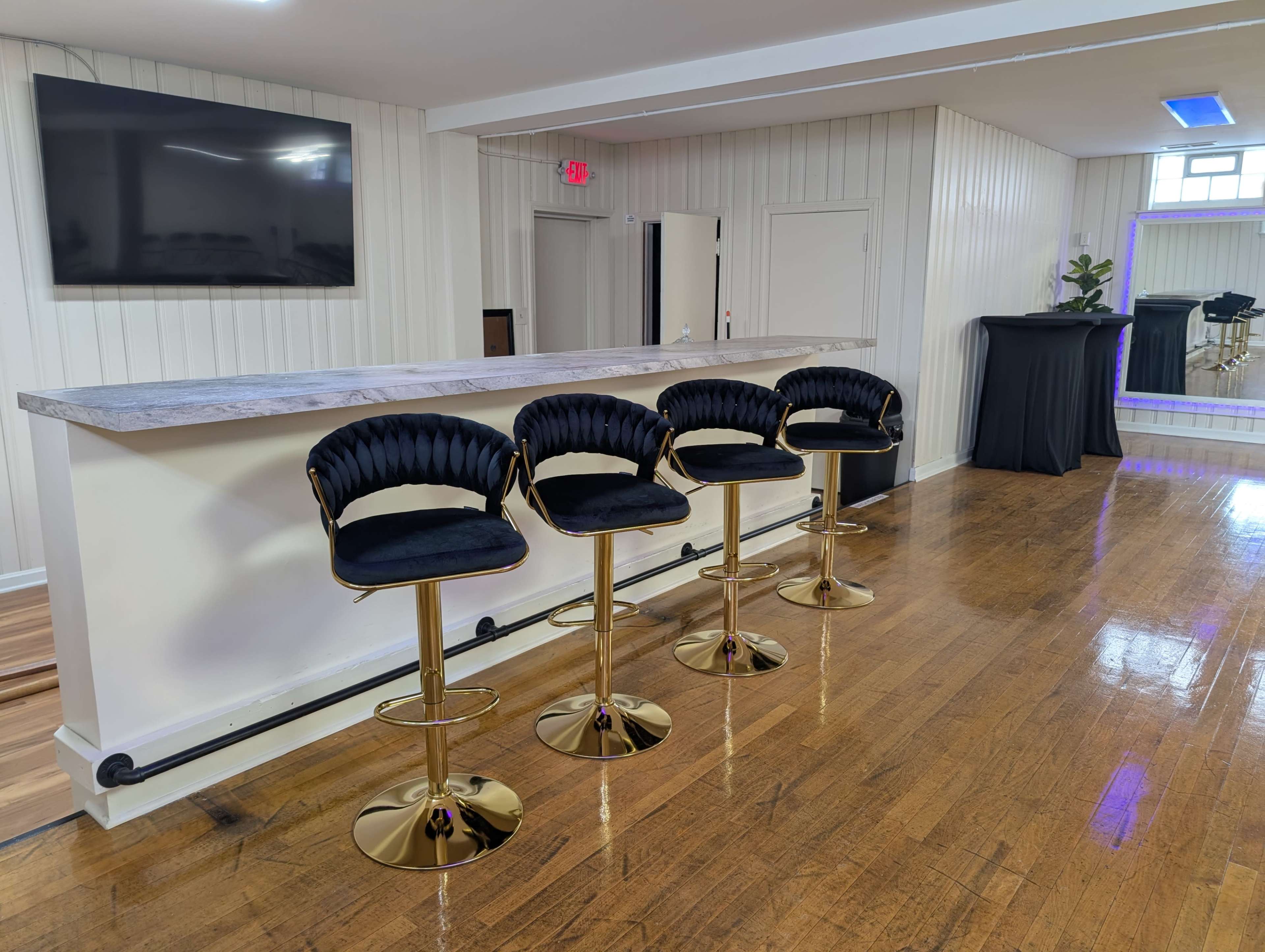 The image shows a modern bar area with four black cushioned stools lined up in front of a marble countertop.