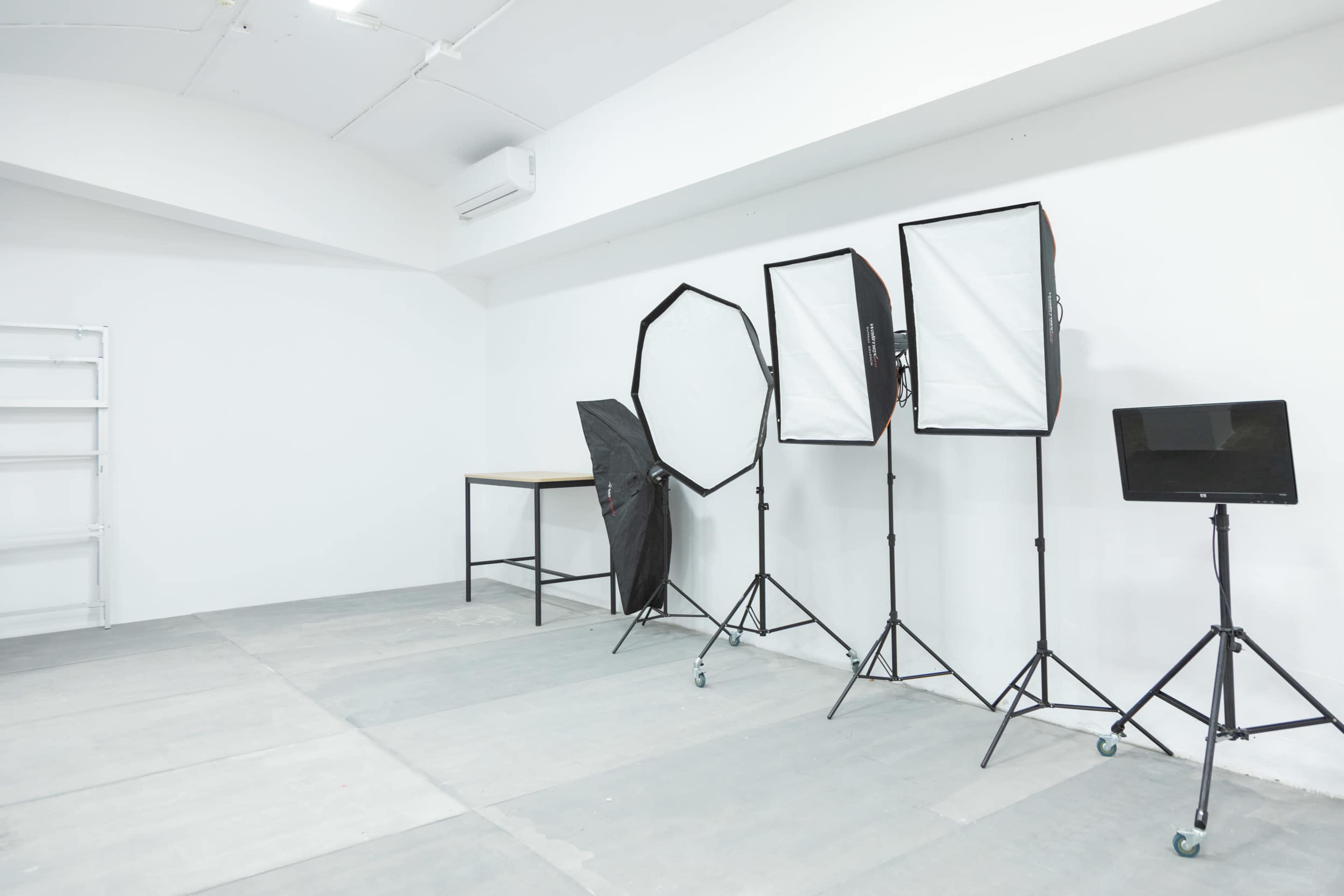 A minimalist photography studio with lighting equipment and a table against a white wall.