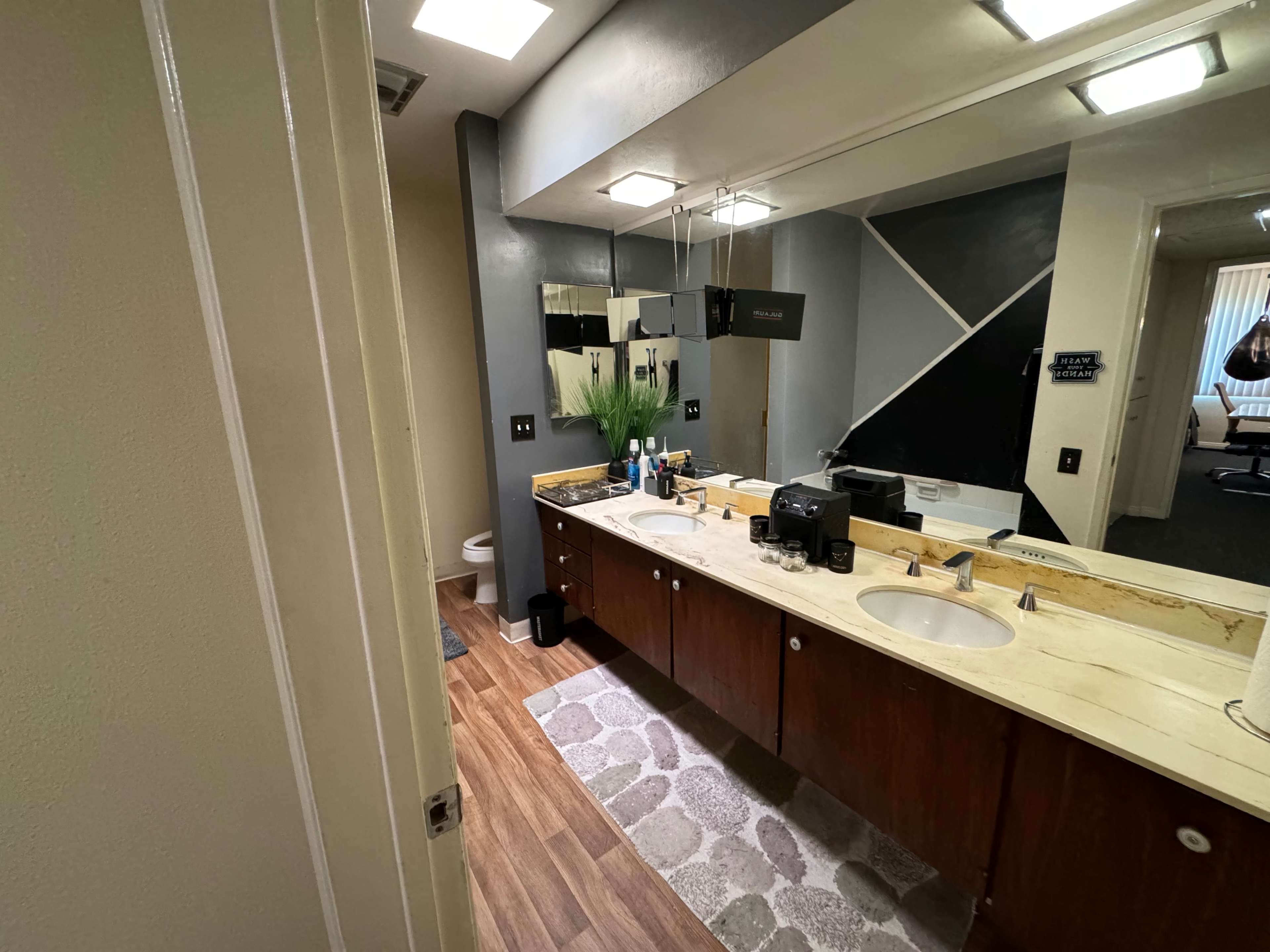 A bathroom with dual sinks, a mirrored wall, and a wooden cabinet along the countertop.