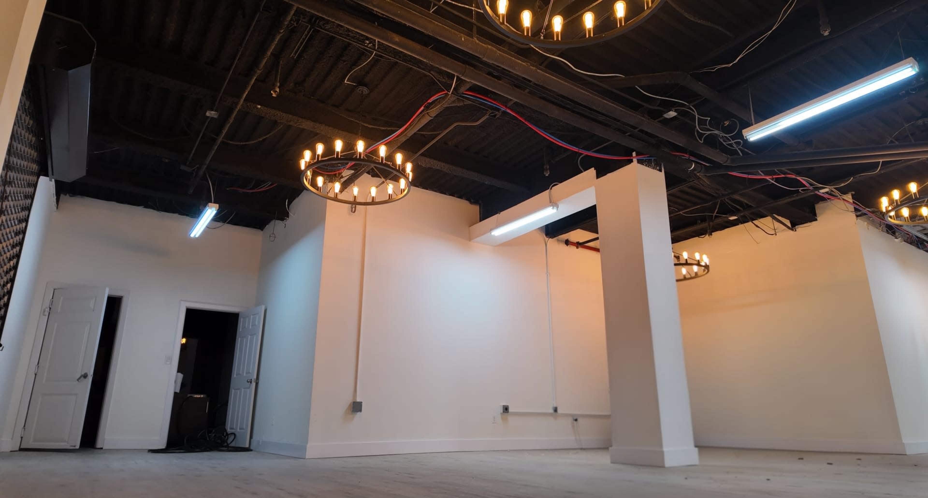 The image shows an empty room with white walls, wooden flooring, and two circular light fixtures hanging from the ceiling.