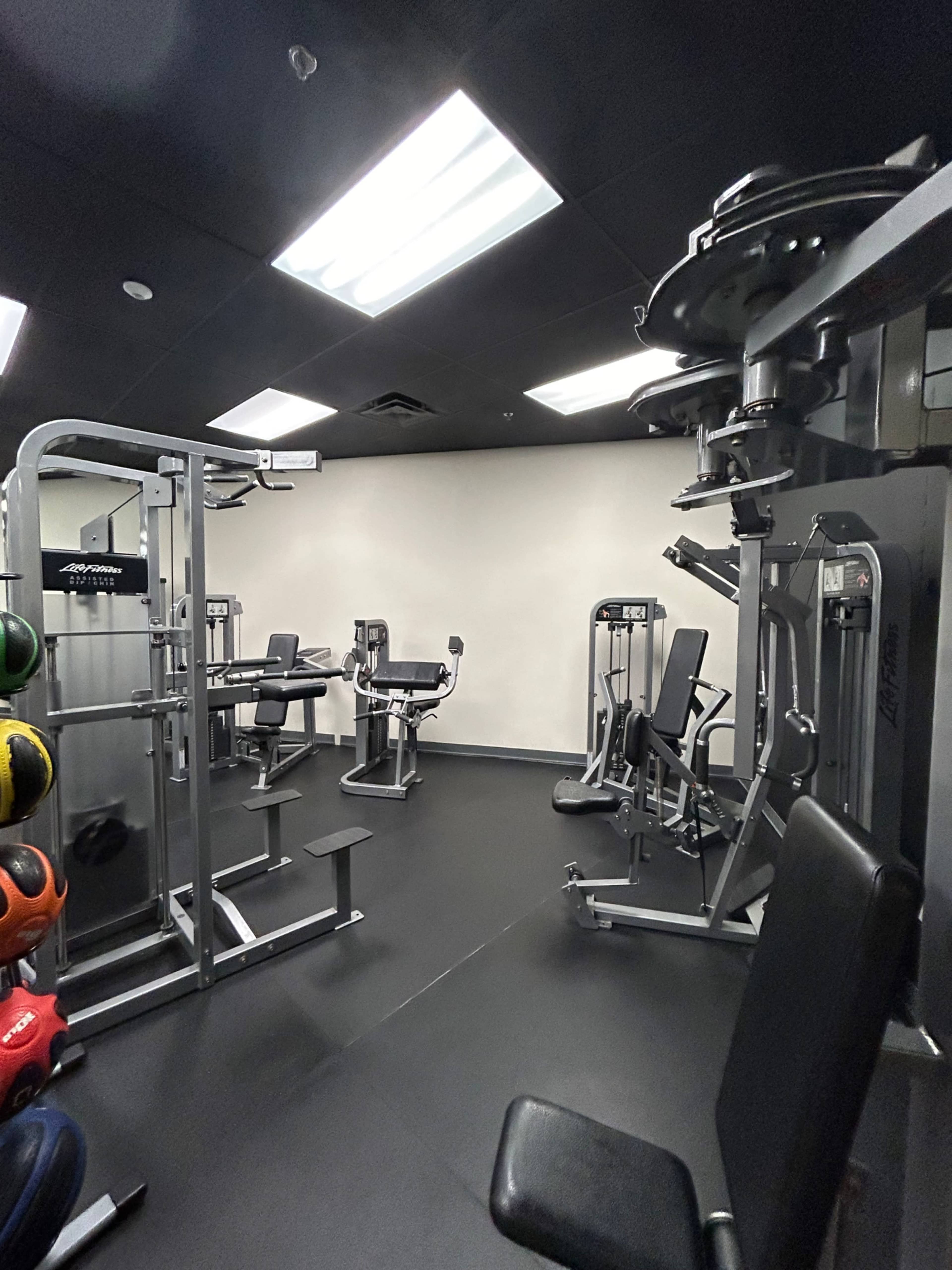 A small gym featuring various weightlifting machines and exercise equipment arranged on a dark floor.