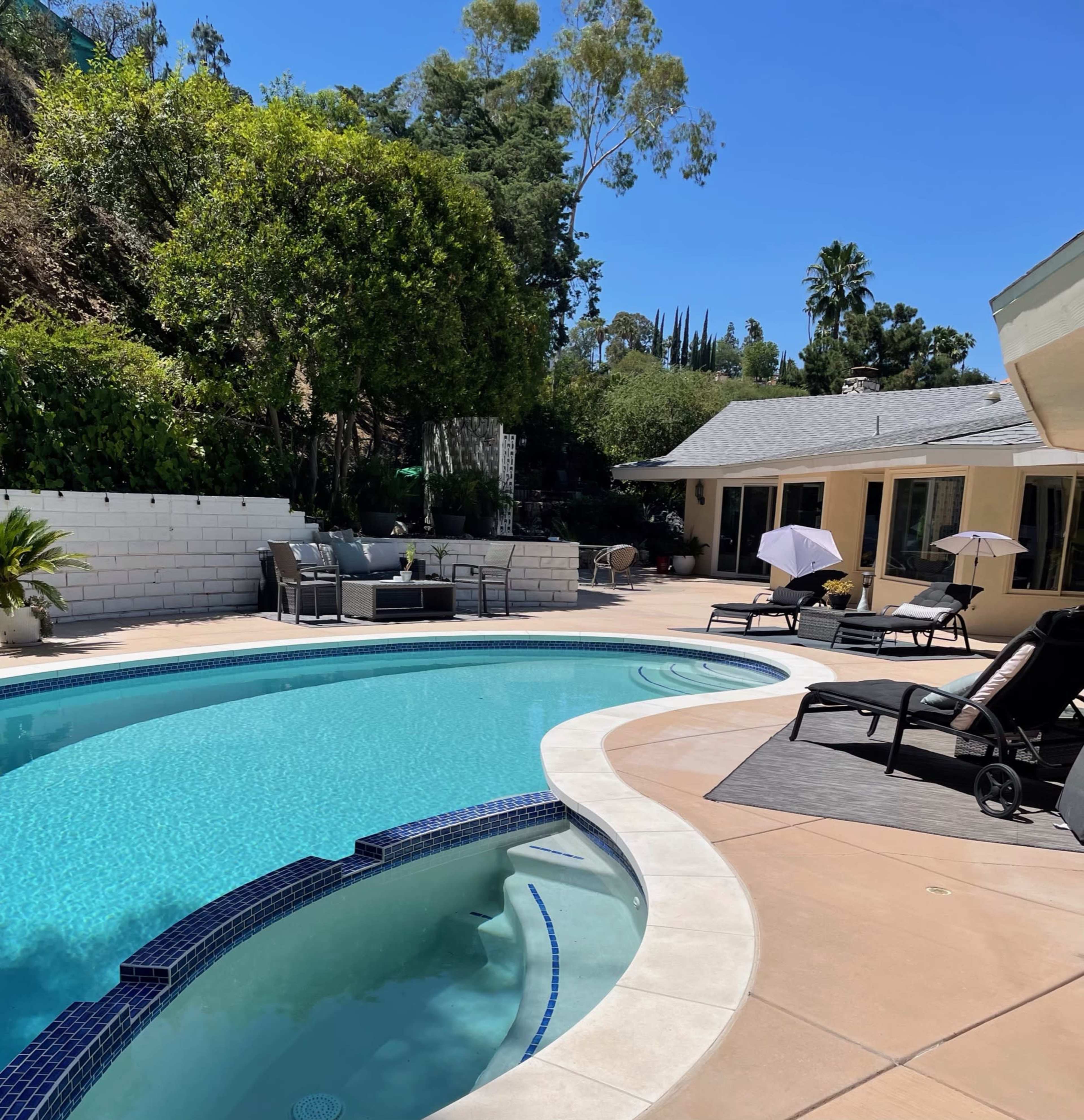 A well-maintained pool area surrounded by lounge chairs and umbrellas in a sunny backyard.