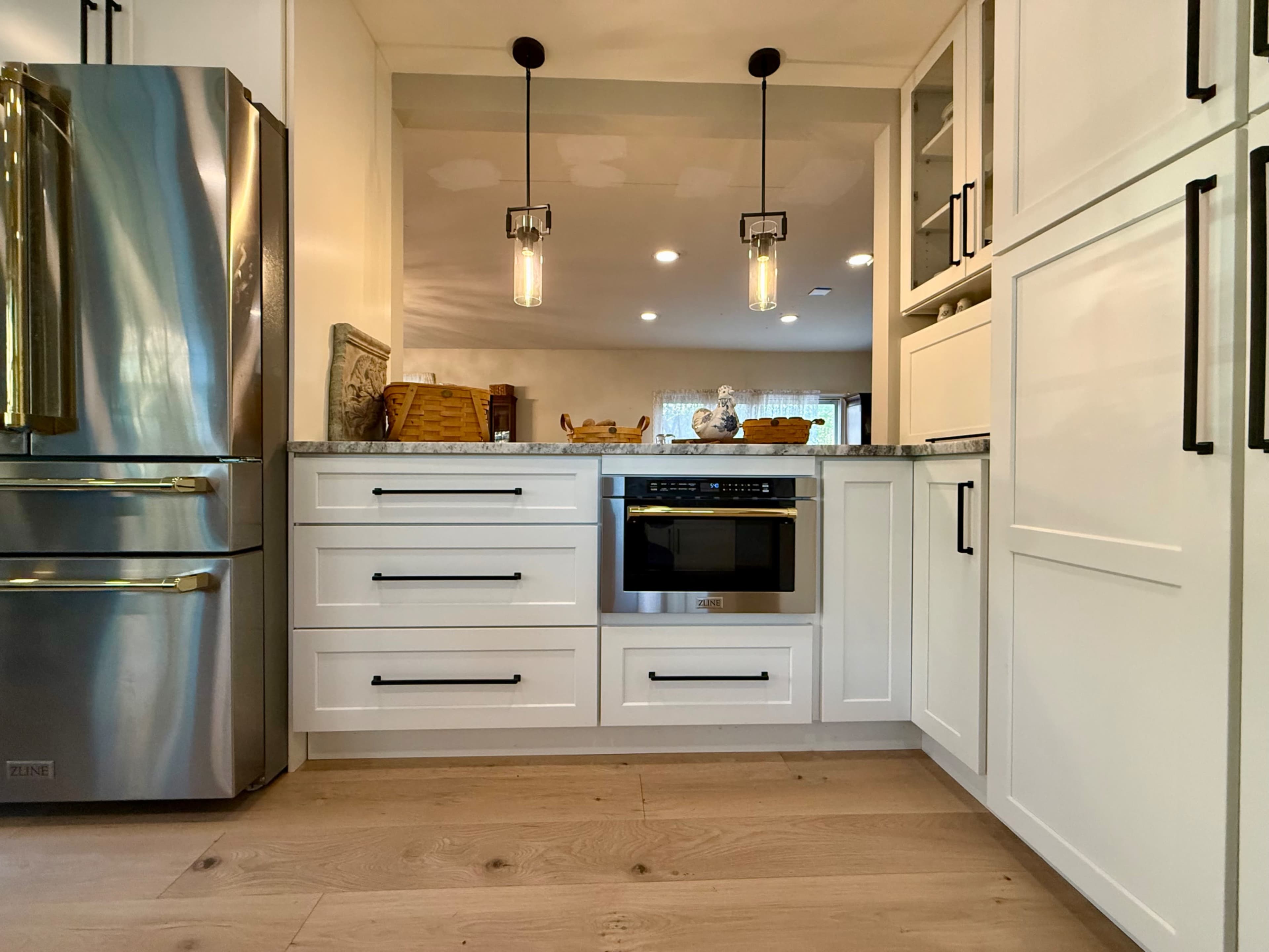 The image shows a modern kitchen with white cabinetry, stainless steel appliances, and light wooden flooring.