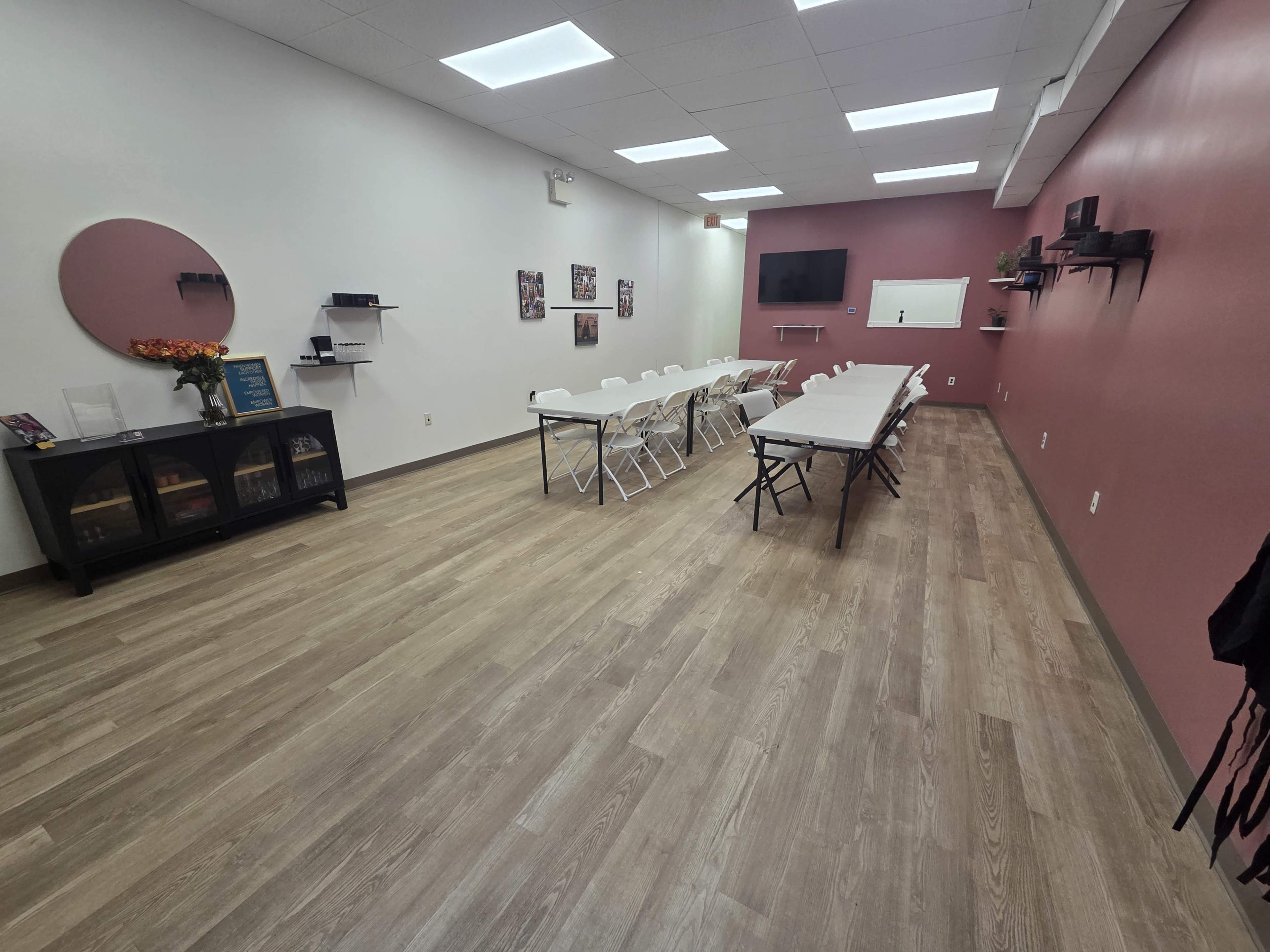 The image shows a spacious meeting room with a long table and chairs arranged in a seminar style, along with a TV and whiteboard mounted on the walls.