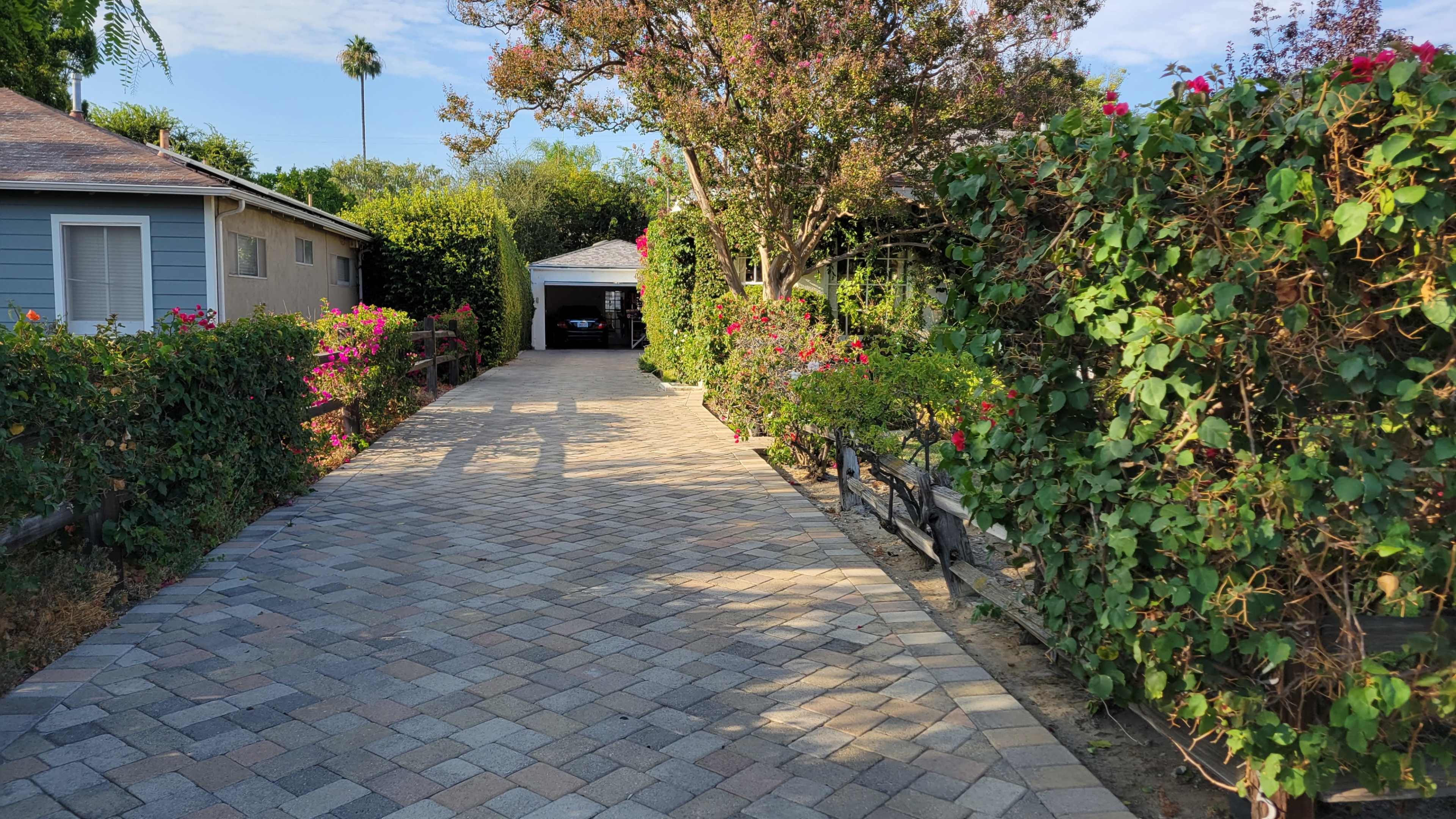 A paved driveway lined with colorful shrubs leads to a garage at the end.