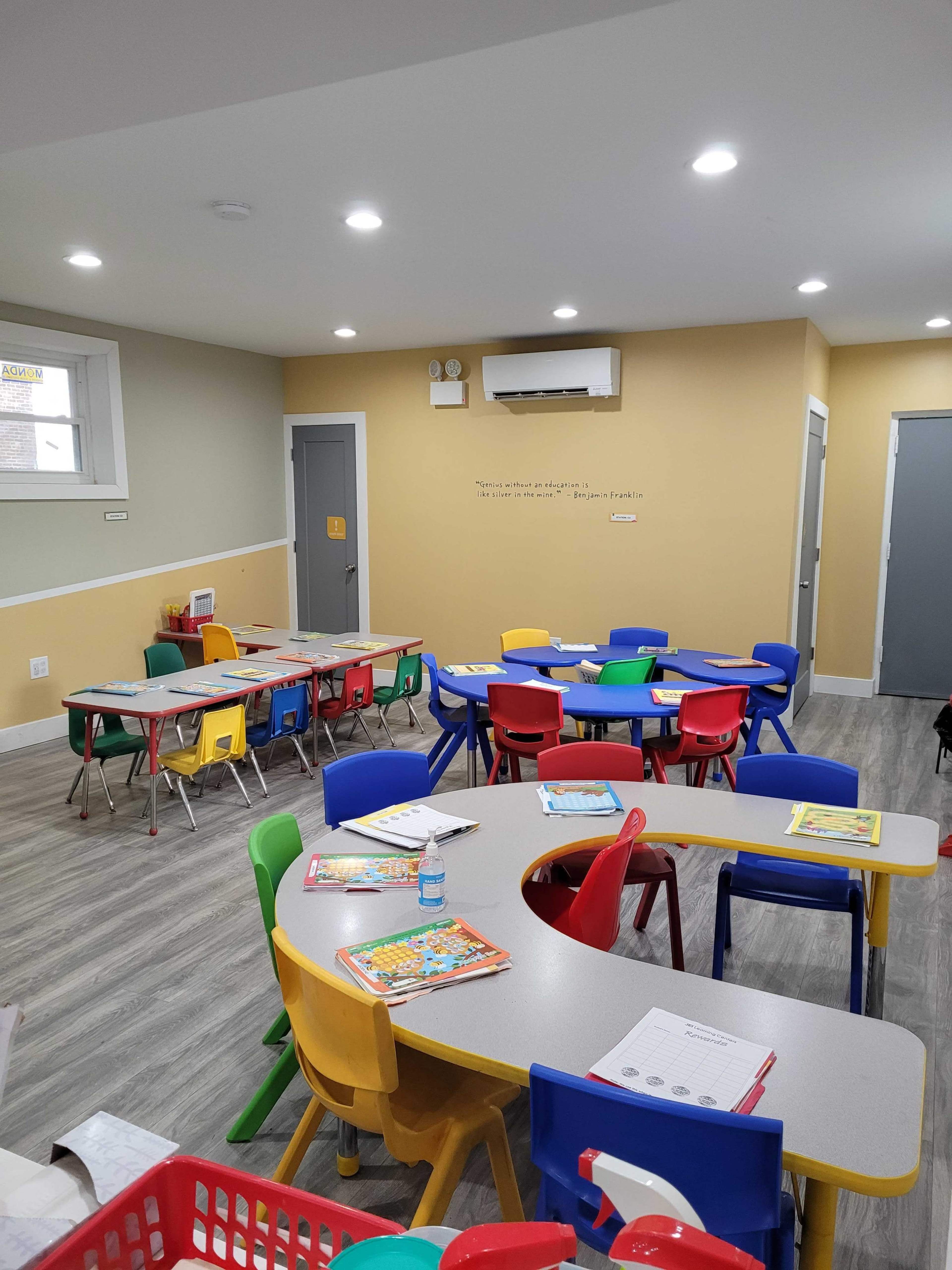 A brightly colored classroom with several round tables surrounded by chairs in various colors, along with educational materials scattered on the tables.