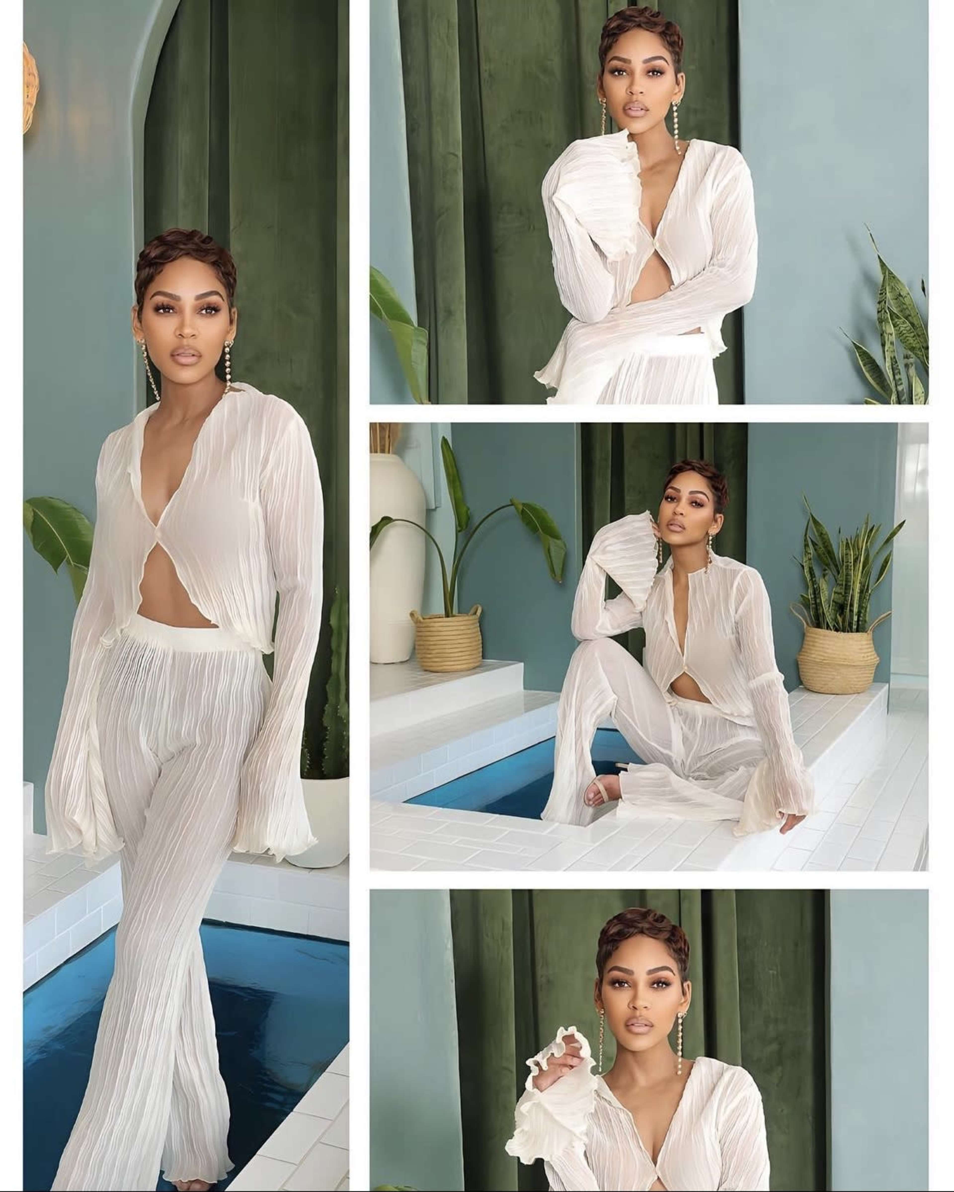 A woman in a white pleated outfit, posing in a stylish indoor setting with plants and a water feature.
