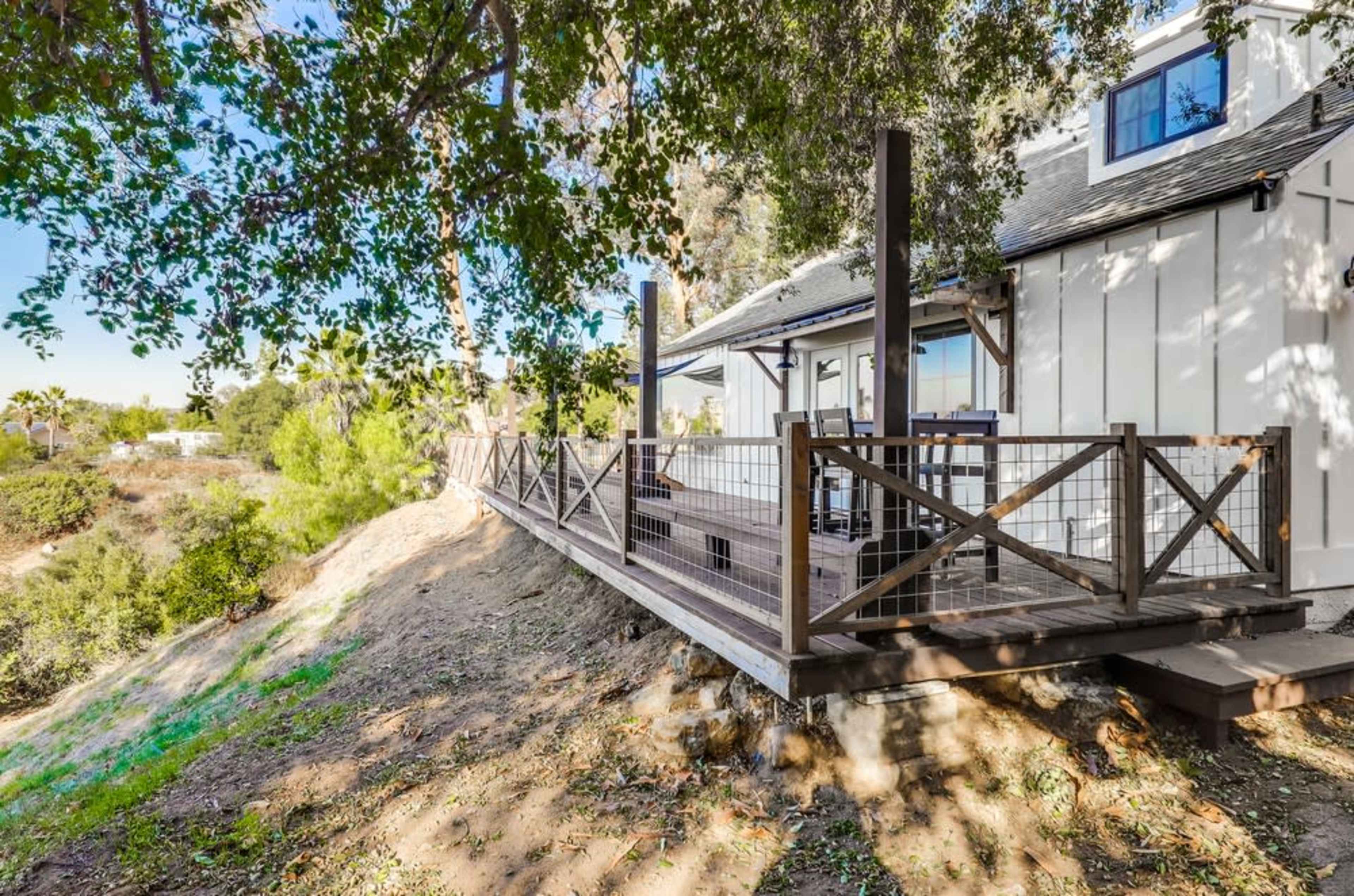 A wooden deck extends from a house, overlooking a hillside covered in greenery.