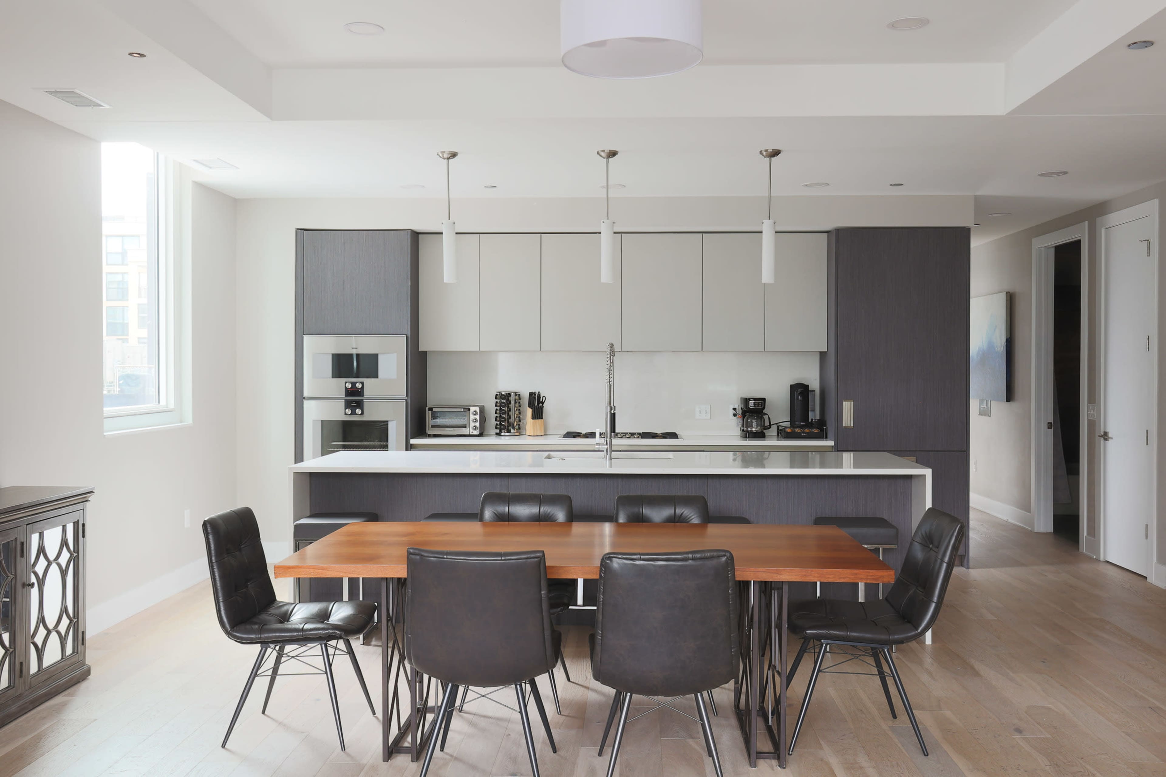 A modern kitchen and dining area with a wooden table surrounded by black chairs, sleek cabinetry, and appliances.