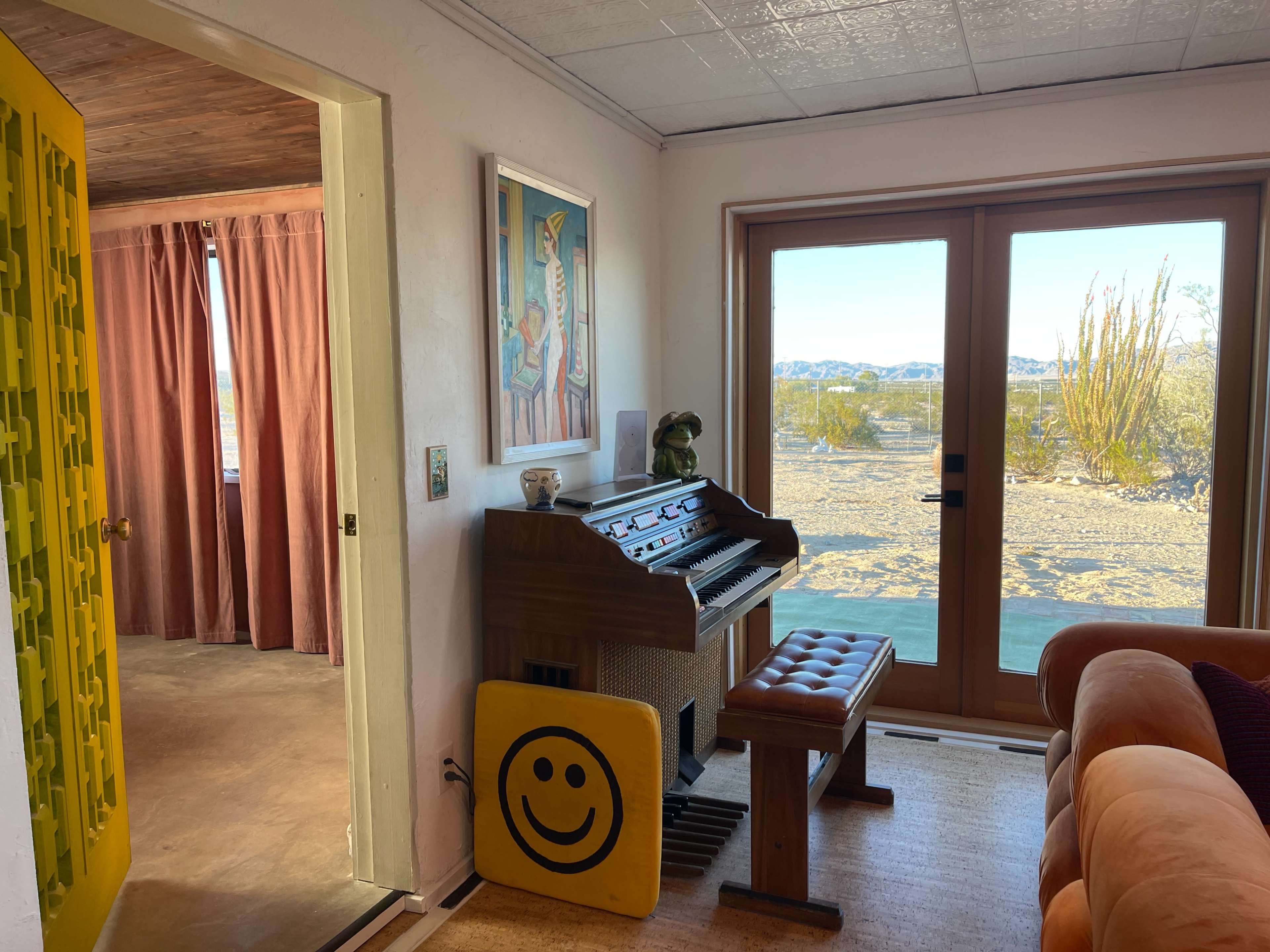 A bright room features an organ, a smiling face sign, and large windows overlooking a desert landscape.