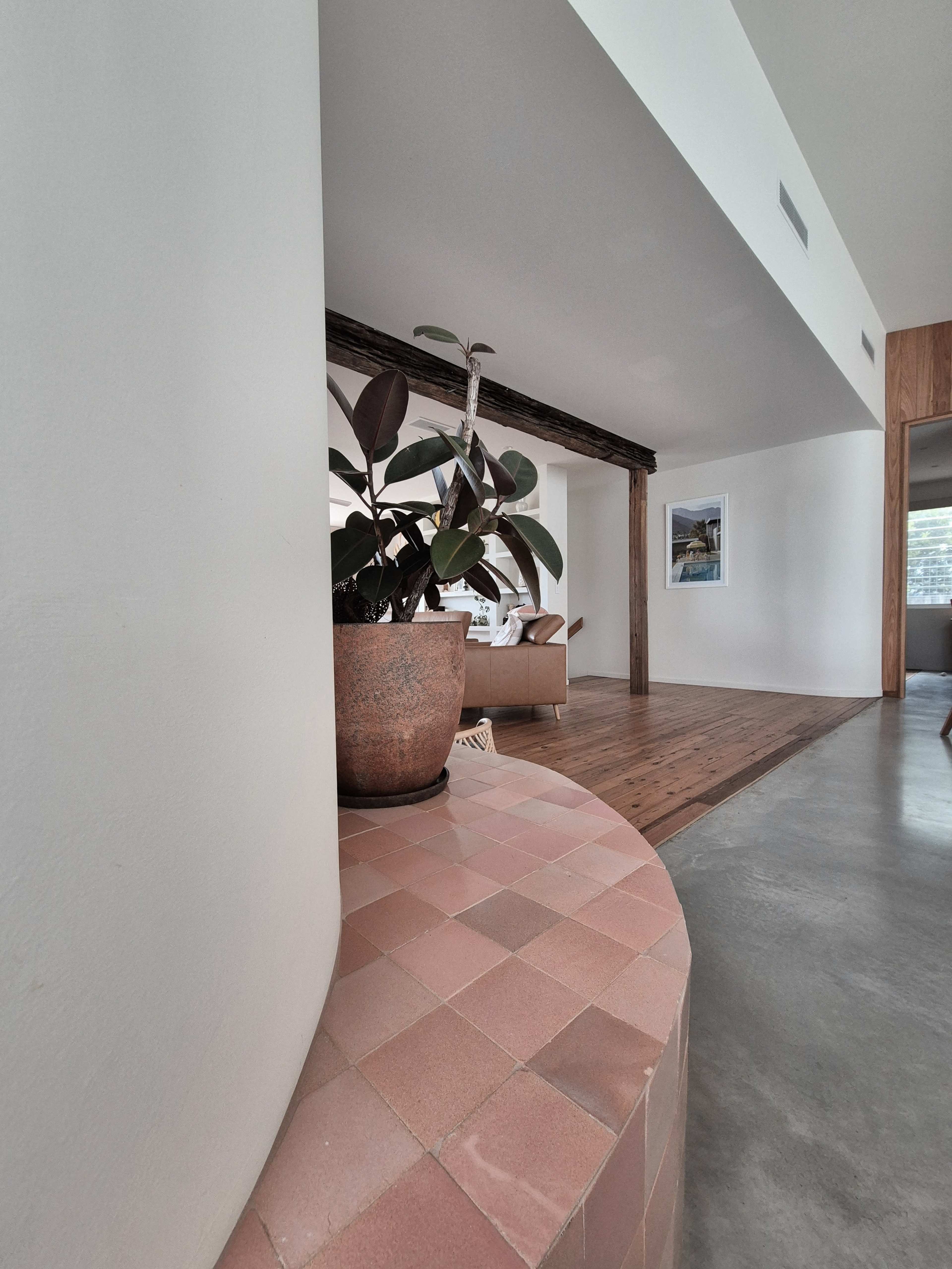The image showcases a modern interior space featuring a curved brick planter with a leafy plant, an adjacent wooden floor, and a glimpse of a cozy seating area in the background.