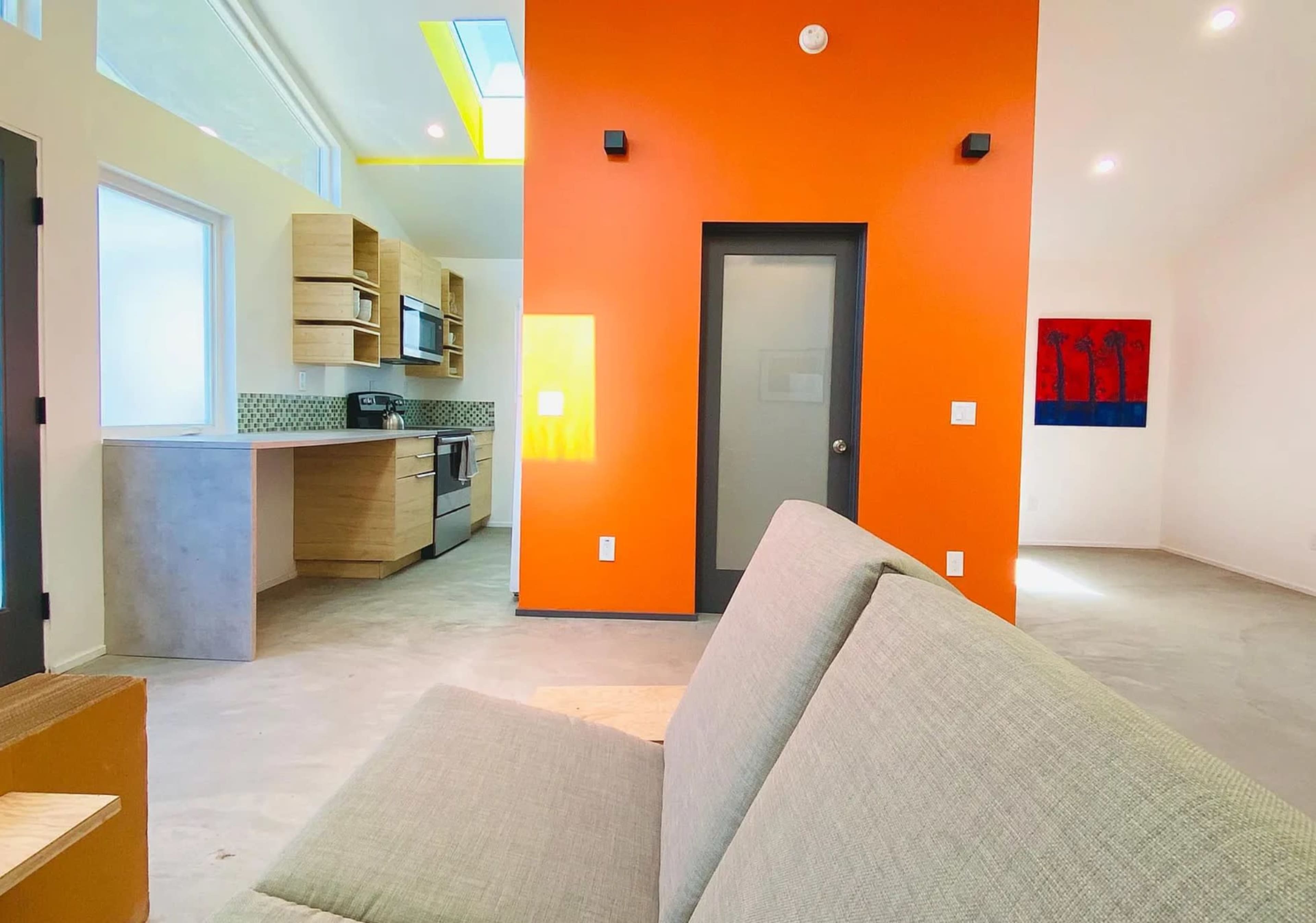 A modern, open-concept living space with a kitchen area on the left and a bright orange accent wall.