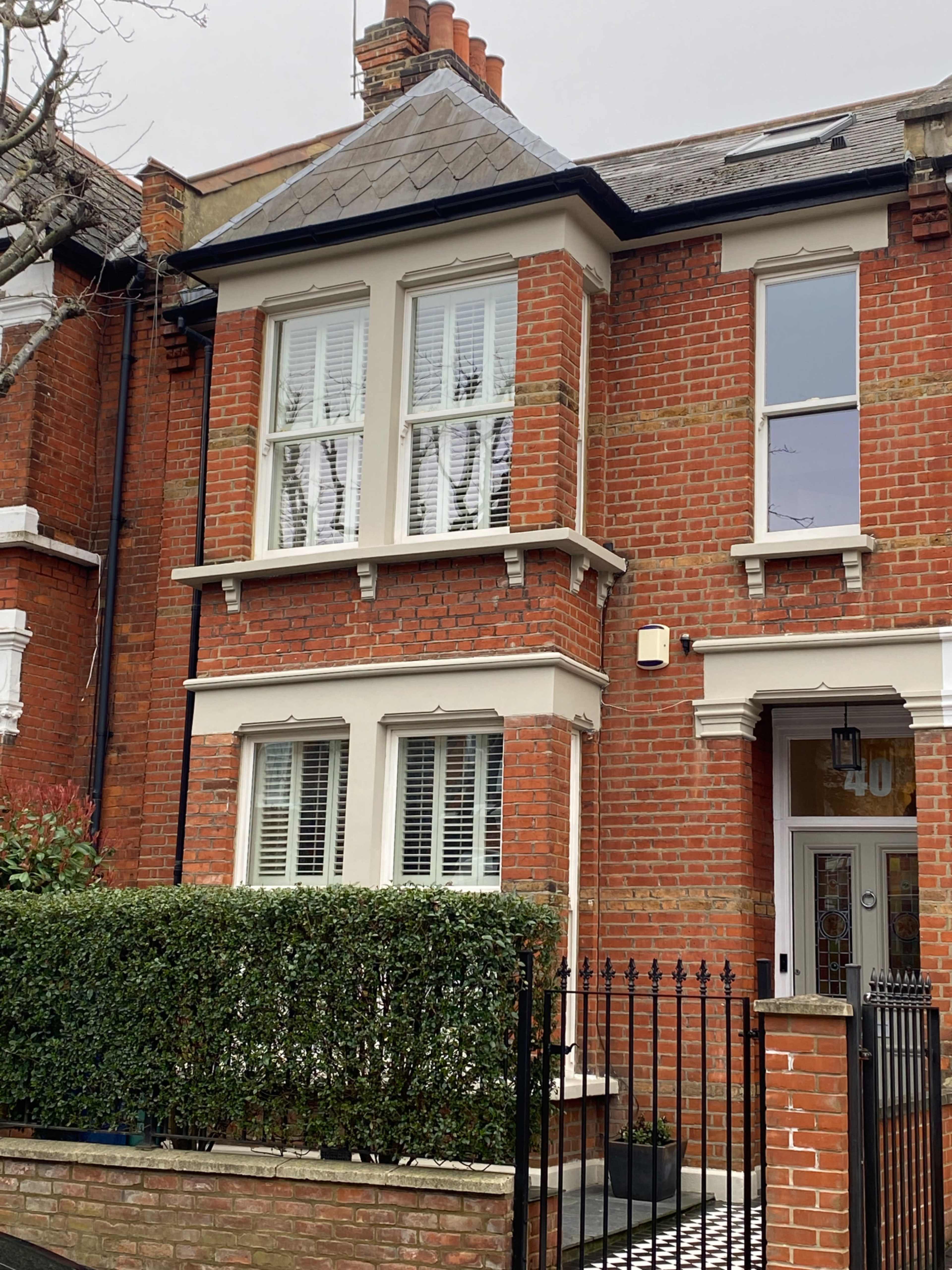 The image shows a brick townhouse with white window shutters and a small garden enclosed by a black wrought-iron fence.