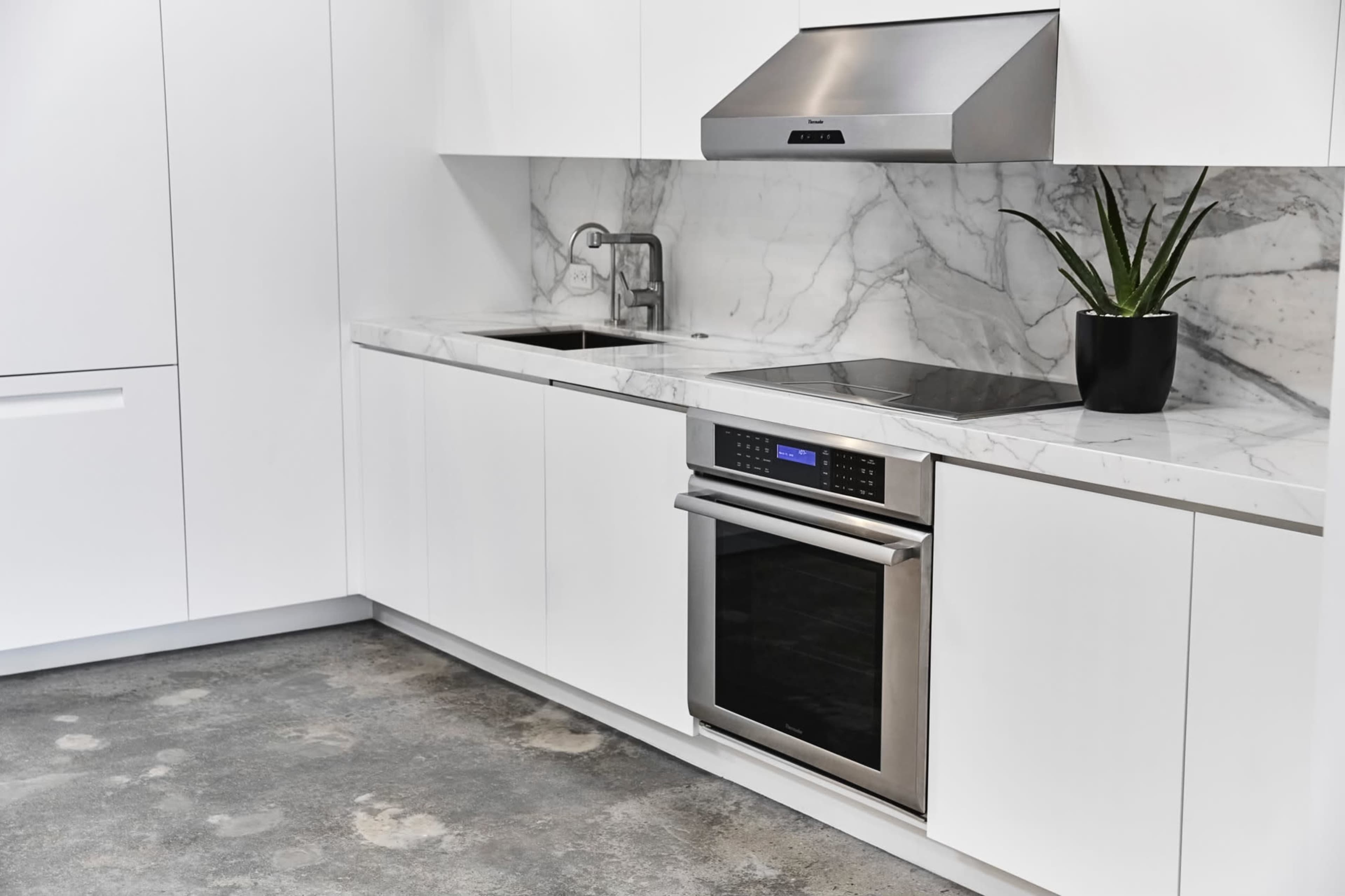 A modern kitchen features white cabinetry, a marble countertop, a stainless steel oven, and a potted plant.