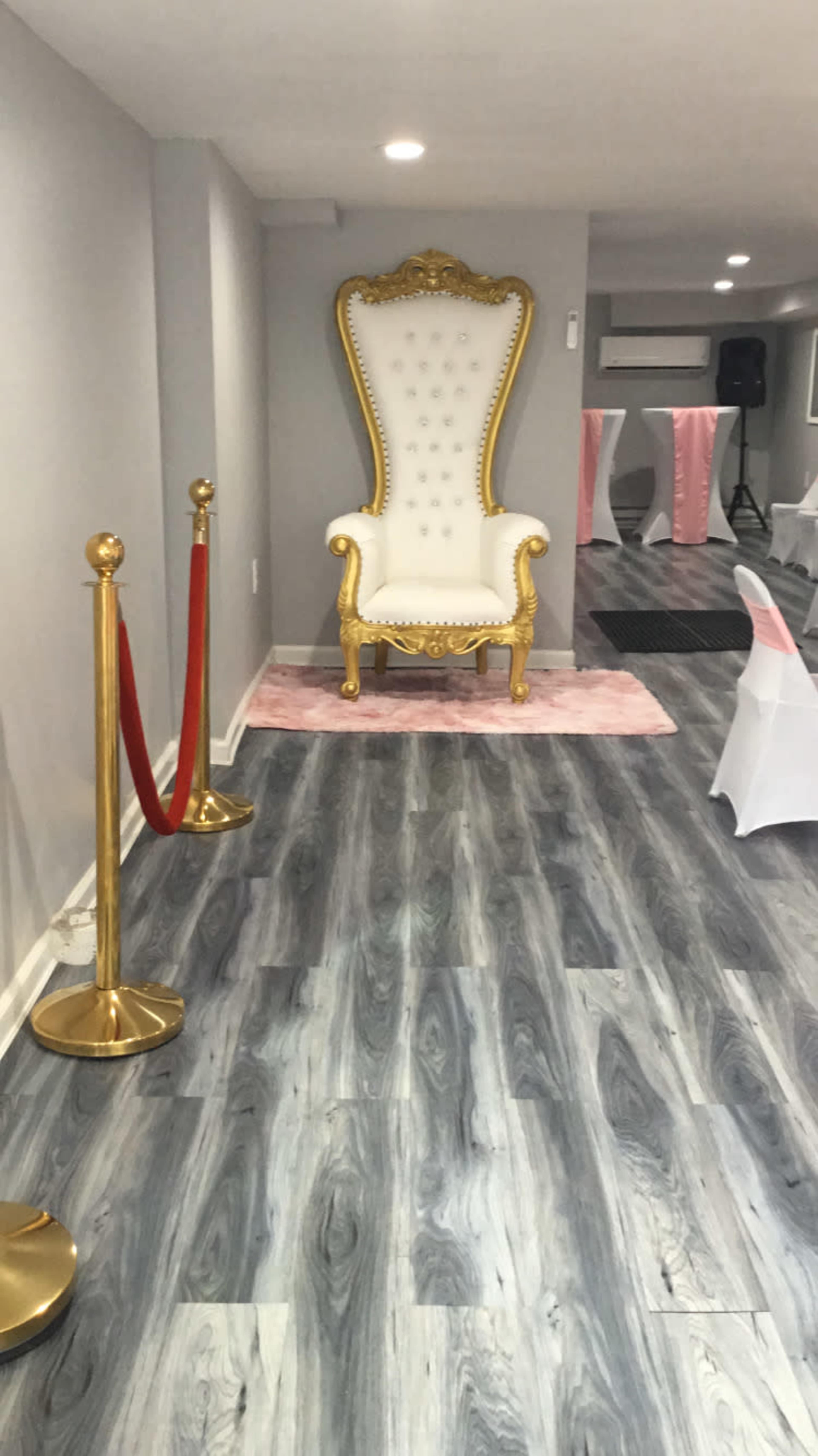 A luxurious white throne with gold accents positioned against a gray wall in a spacious, elegantly decorated room with a wooden floor.