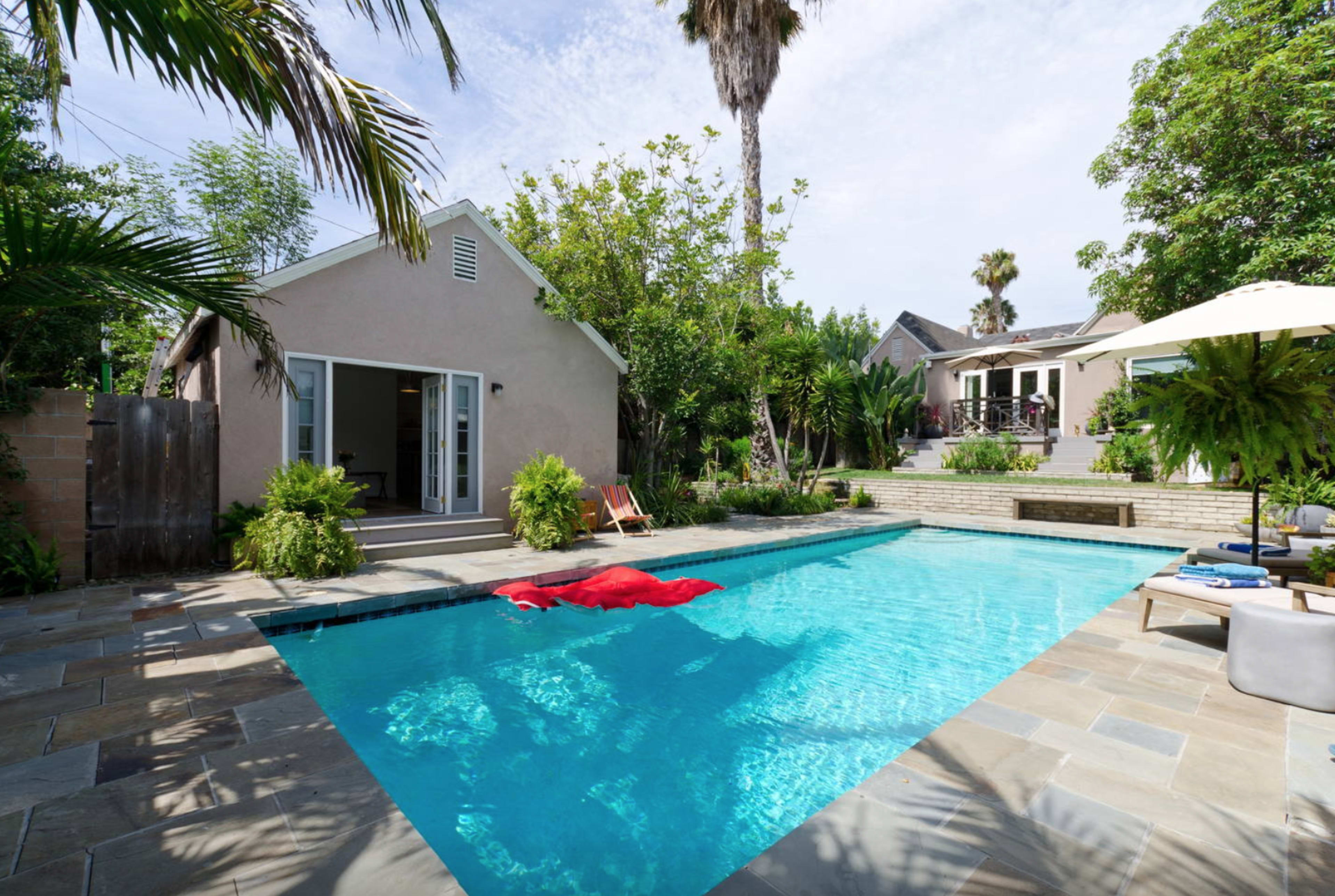 A swimming pool with a red float is surrounded by tropical plants and houses, creating a tranquil outdoor space.