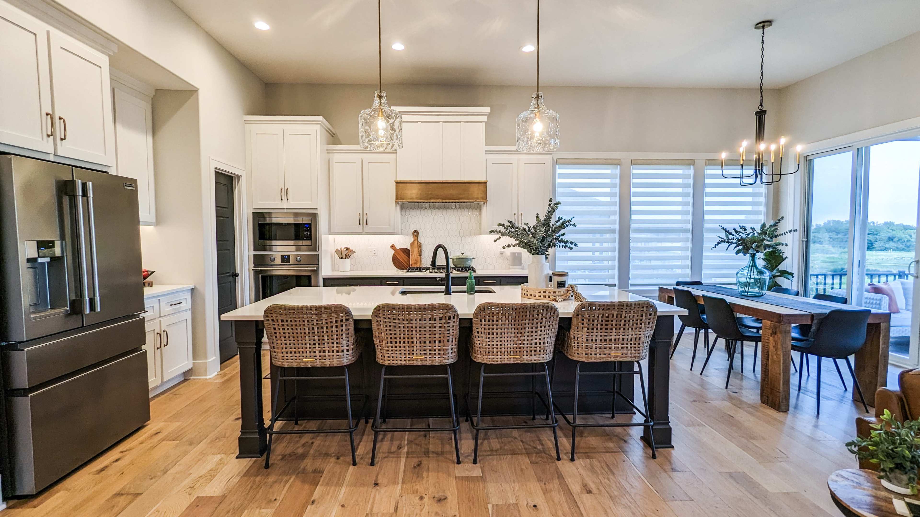 A modern kitchen with white cabinetry, a large island with barstools, and a dining area featuring a table and chairs near large windows.
