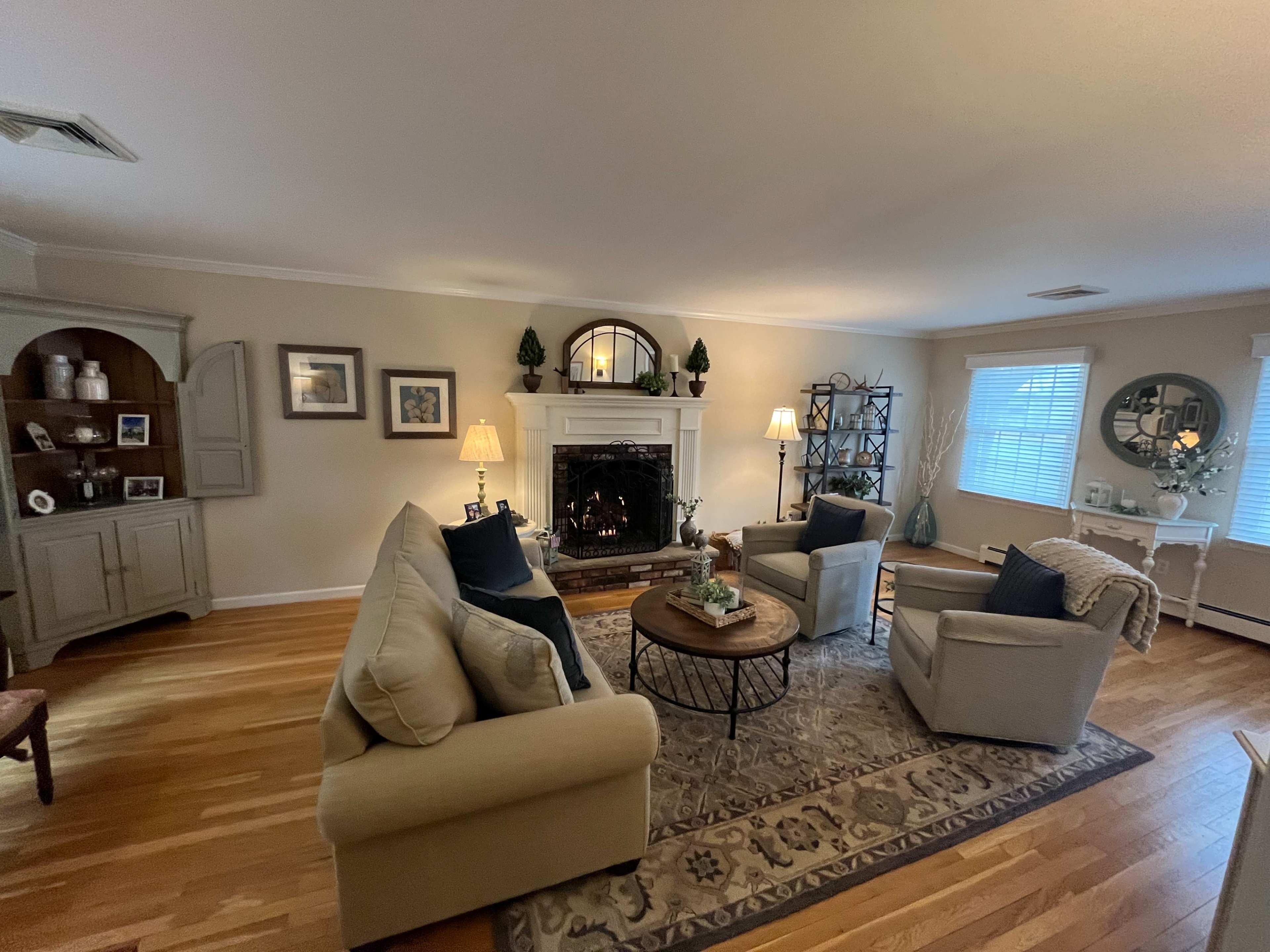 The living room features two beige sofas and a round coffee table arranged around a fireplace, with light-colored walls and hardwood flooring.