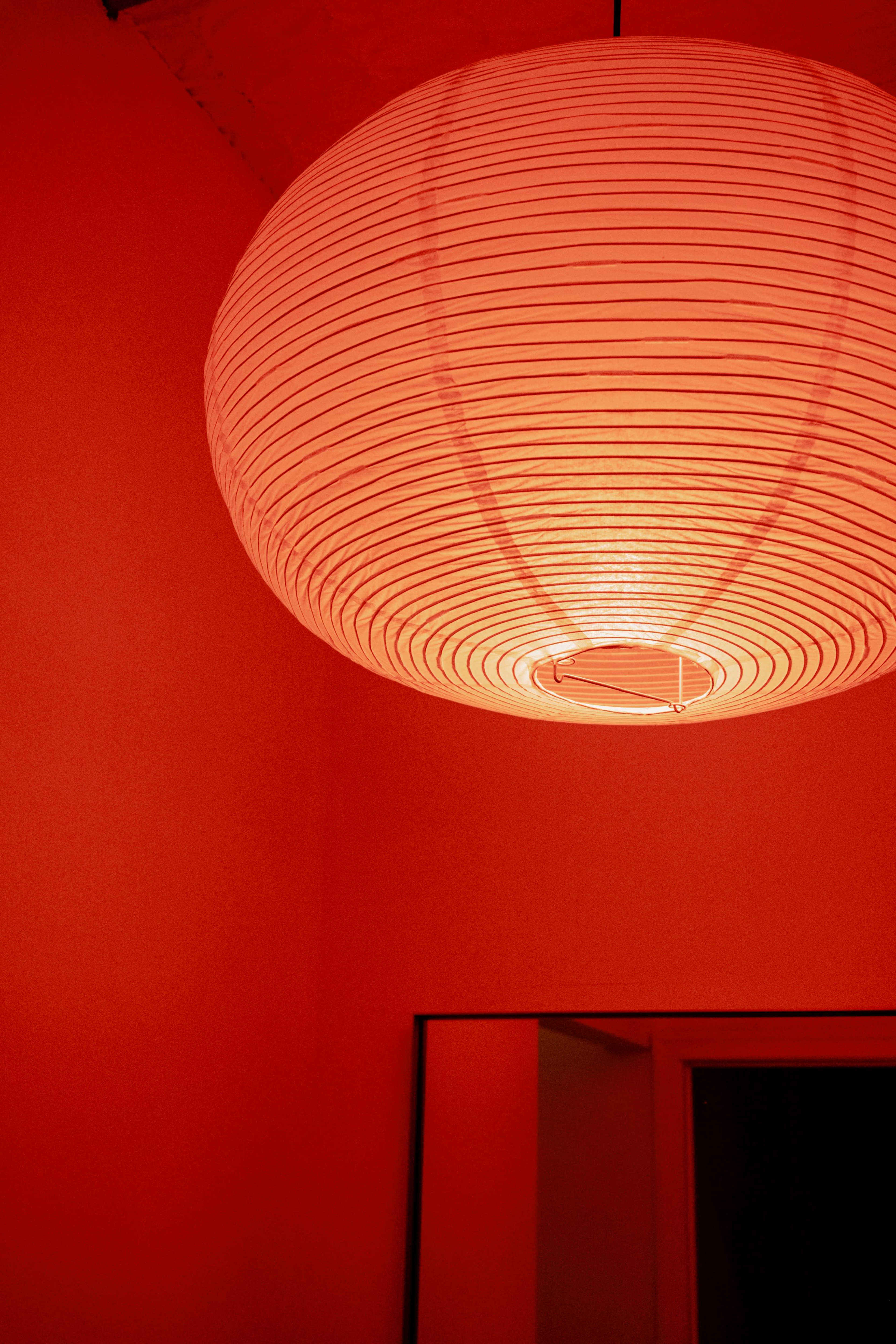 A large, round paper lantern hangs from the ceiling in a red-painted room.
