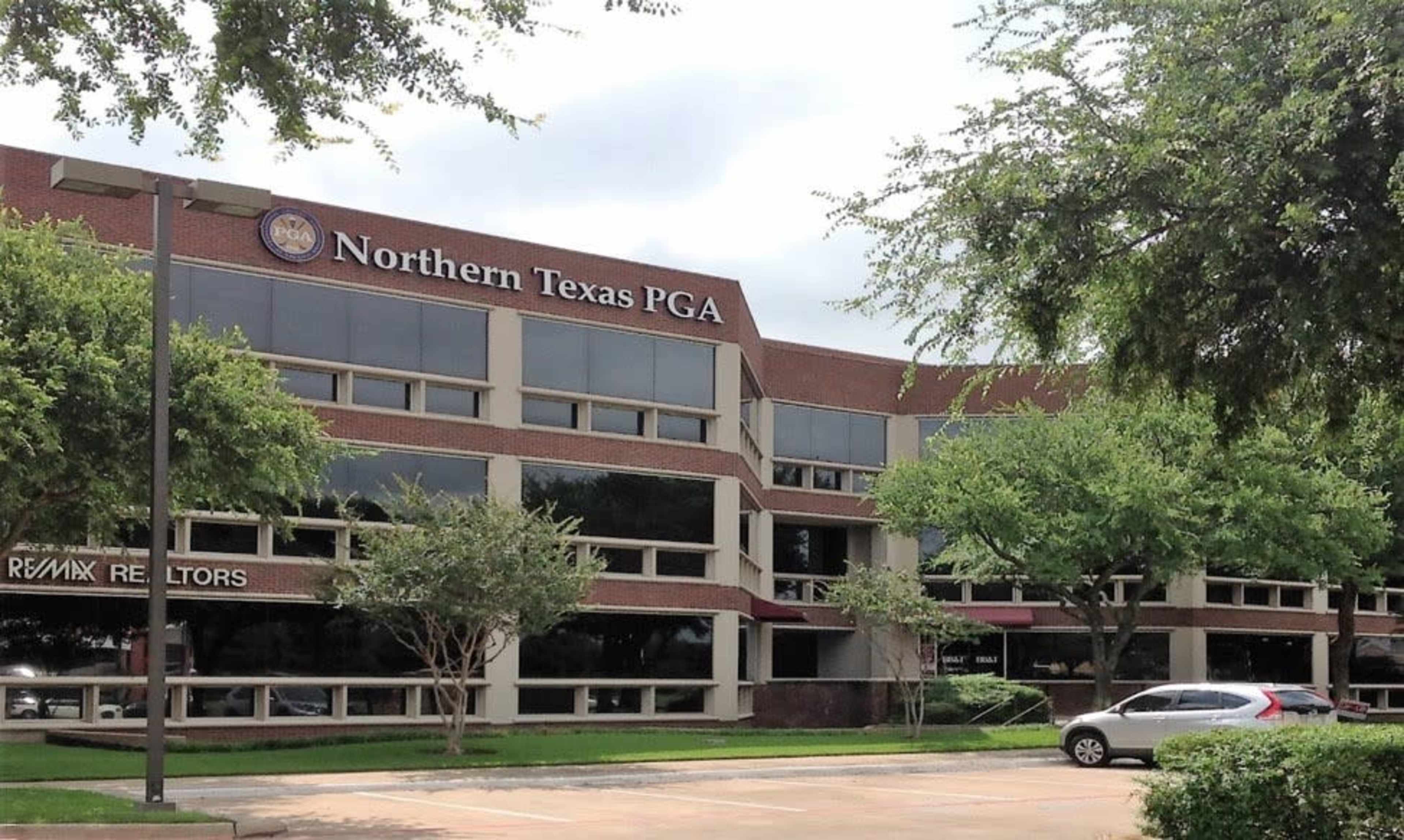 A modern brick building with the sign "Northern Texas PGA" prominently displayed, surrounded by trees and a parking lot.
