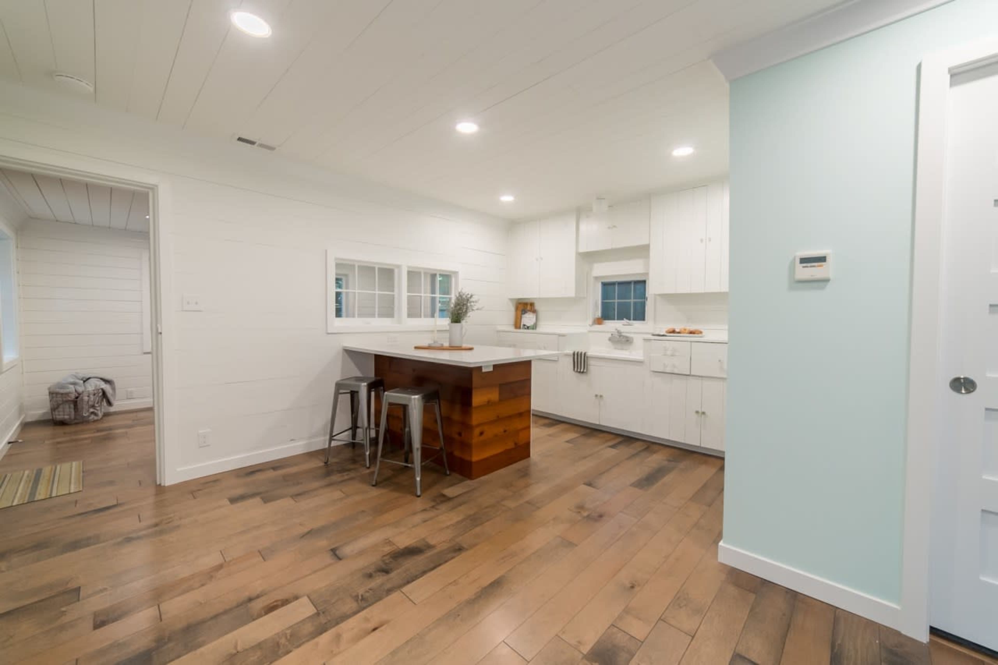 A modern kitchen with white cabinets, a wooden island, and hardwood floors, illuminated by overhead lights.