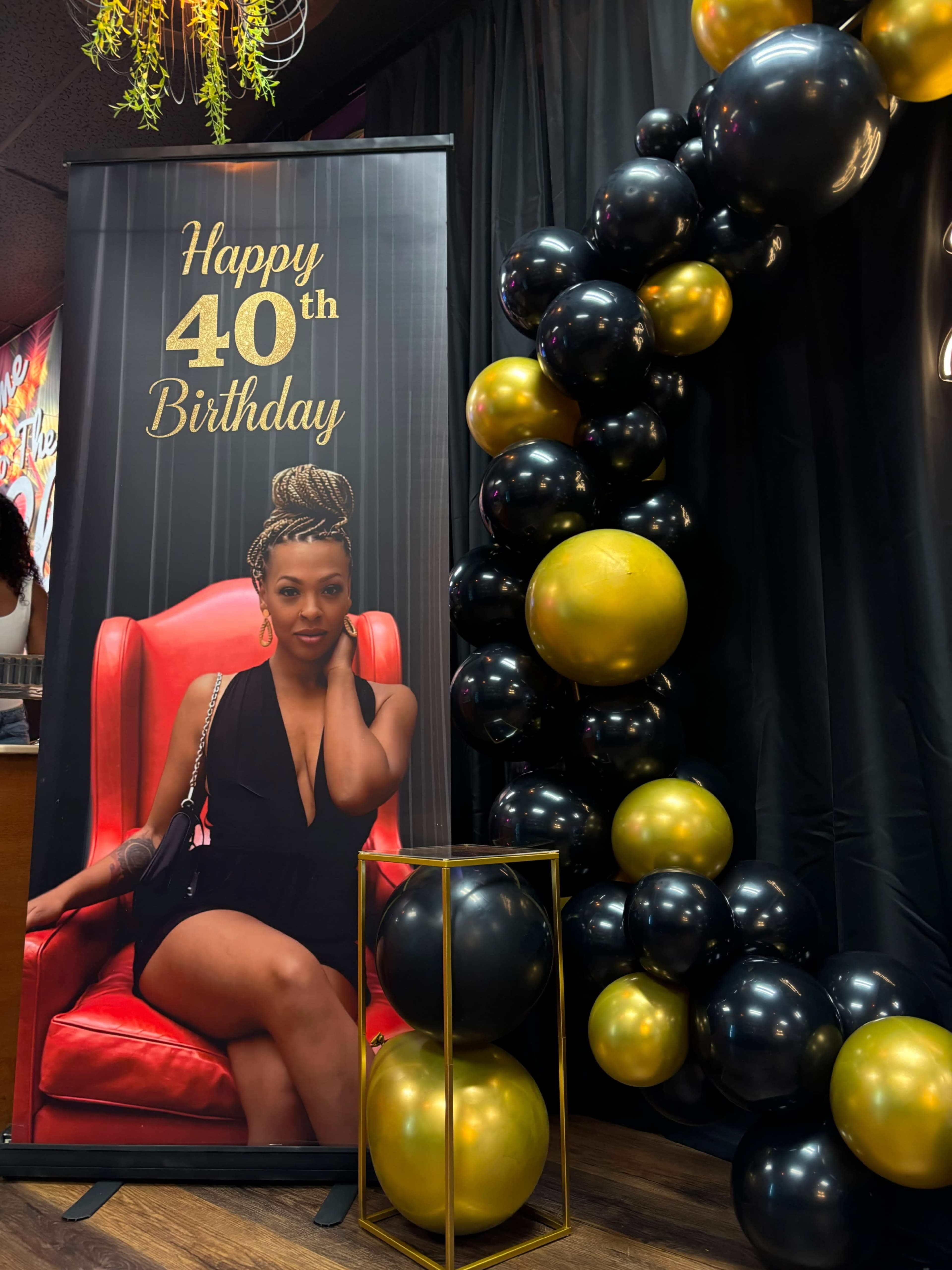 A large banner displays a woman sitting in a red chair with a "Happy 40th Birthday" message, alongside a balloon arrangement in black and gold.