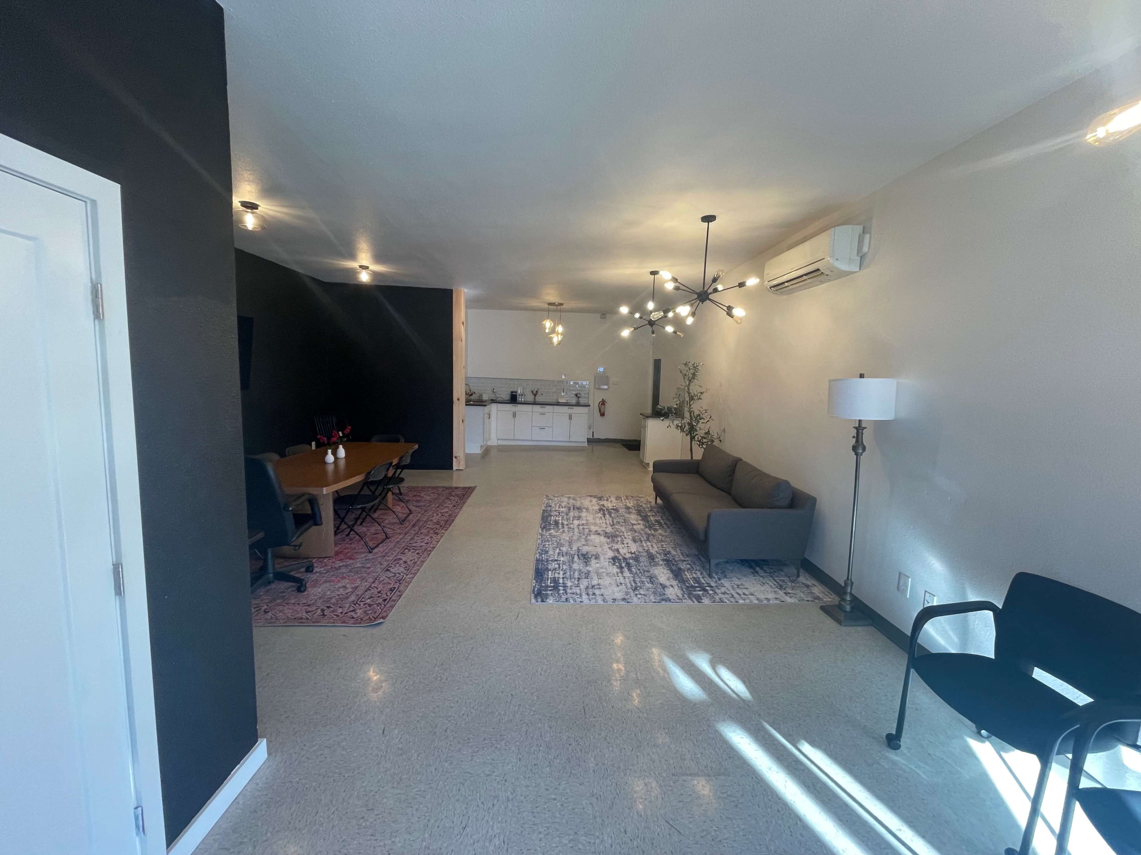 The image shows a modern, open-concept living space with a kitchen, dining area, and a seating area featuring a couch and decorative elements.