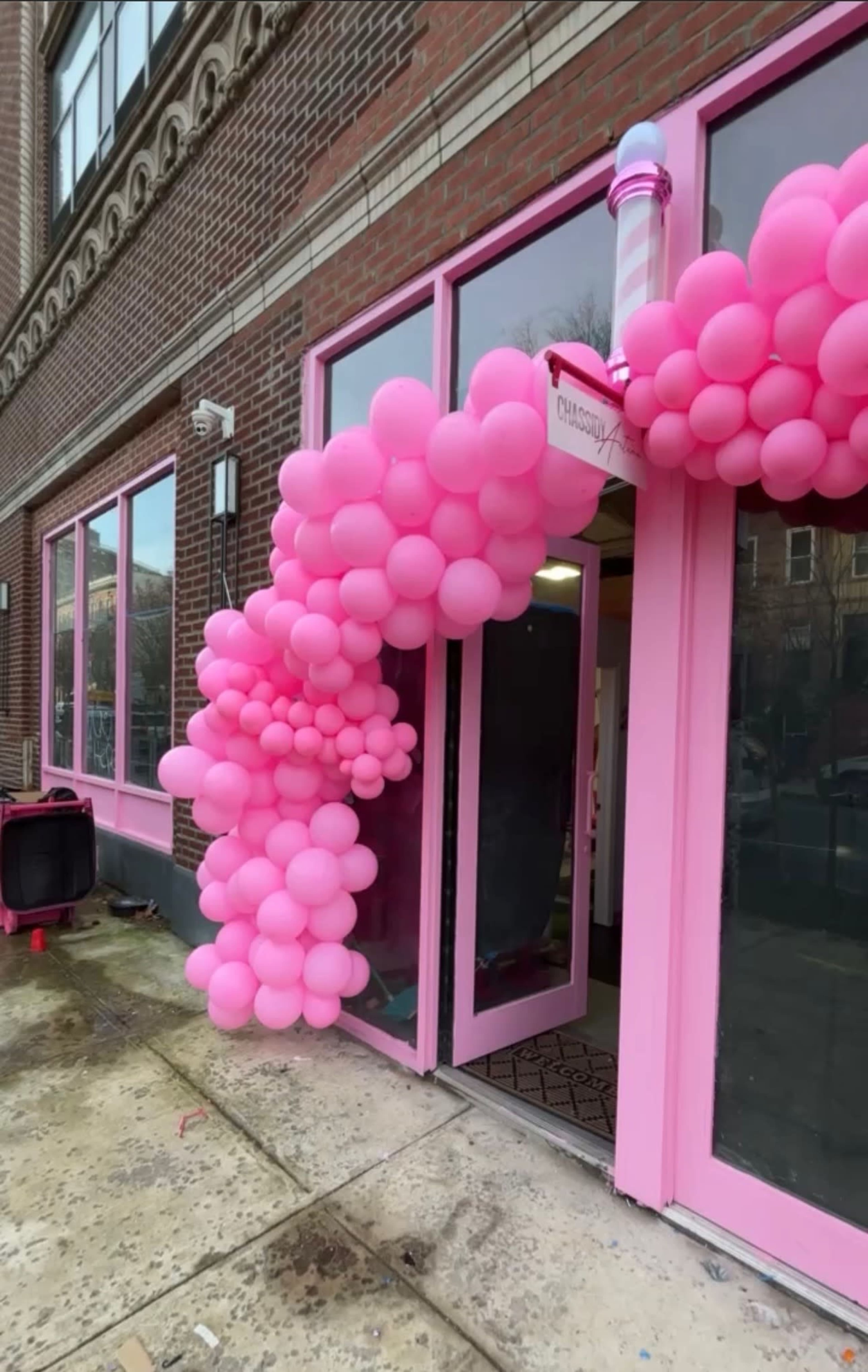 A cluster of pink balloons decorates the entrance of a building, spilling over the door and onto the sidewalk.