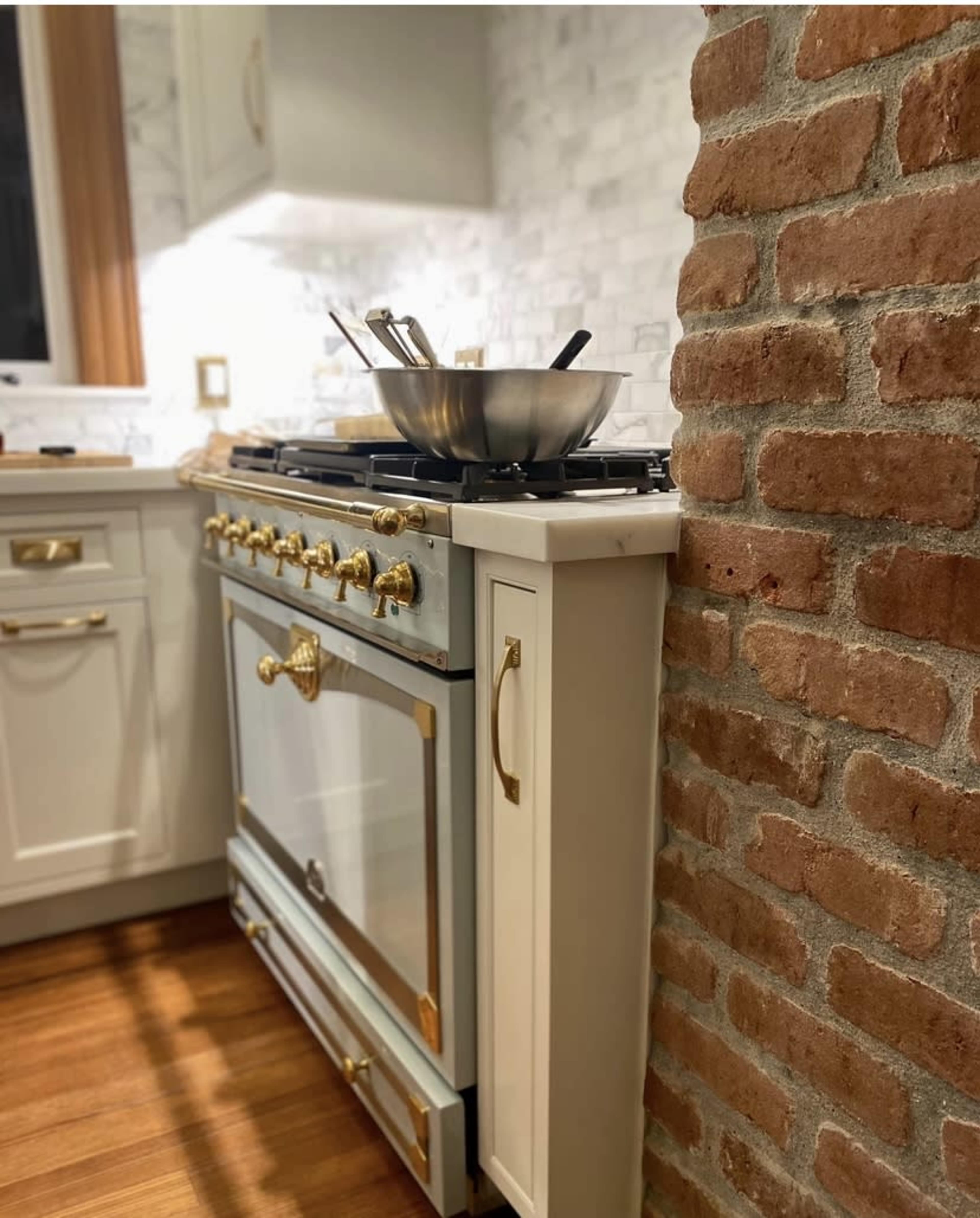 A stainless steel gas stove with a gold-accented design is positioned beside a textured brick wall in a modern kitchen.