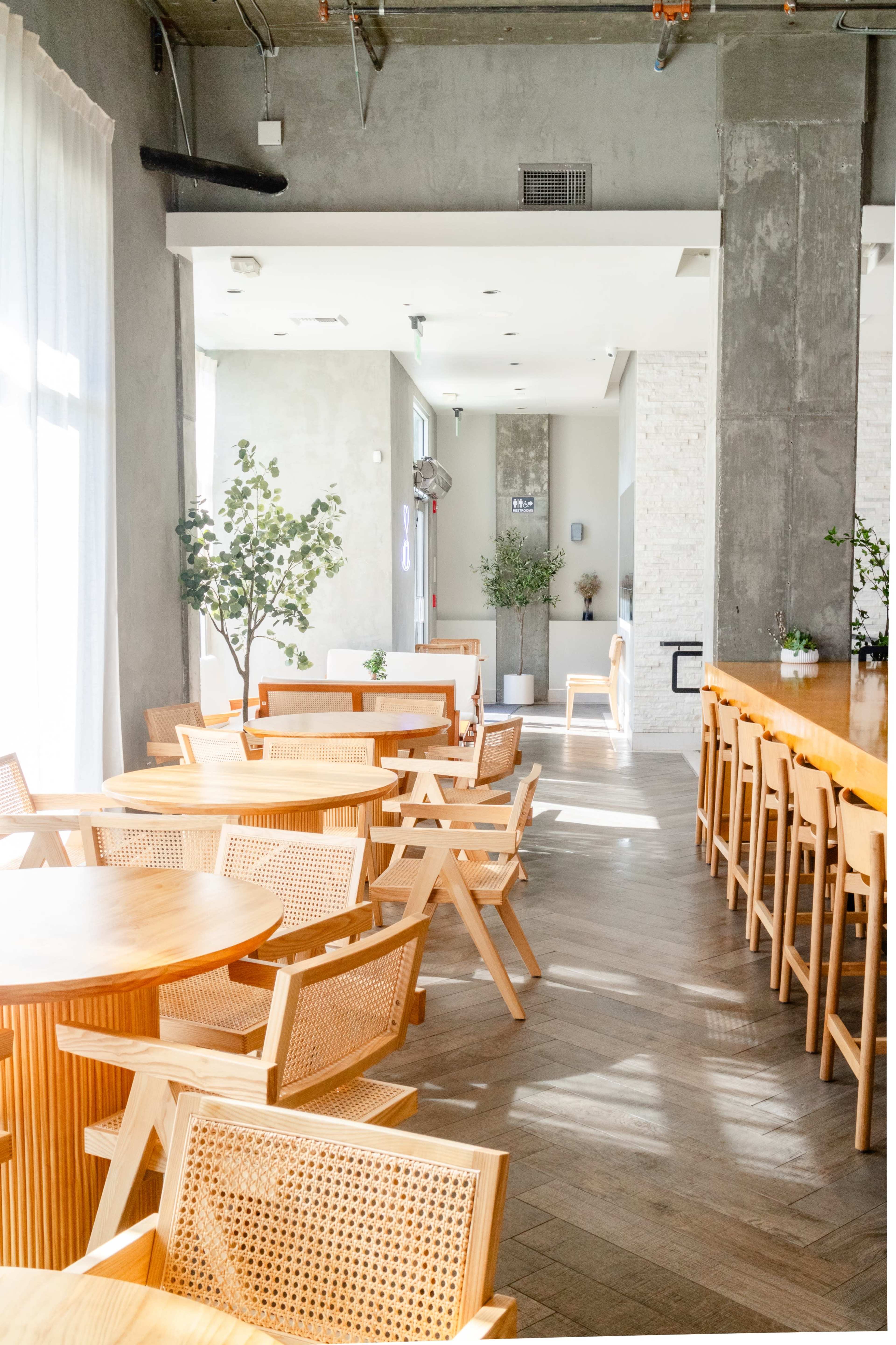 A contemporary dining space with wooden tables, woven chairs, and natural light streaming through large windows.