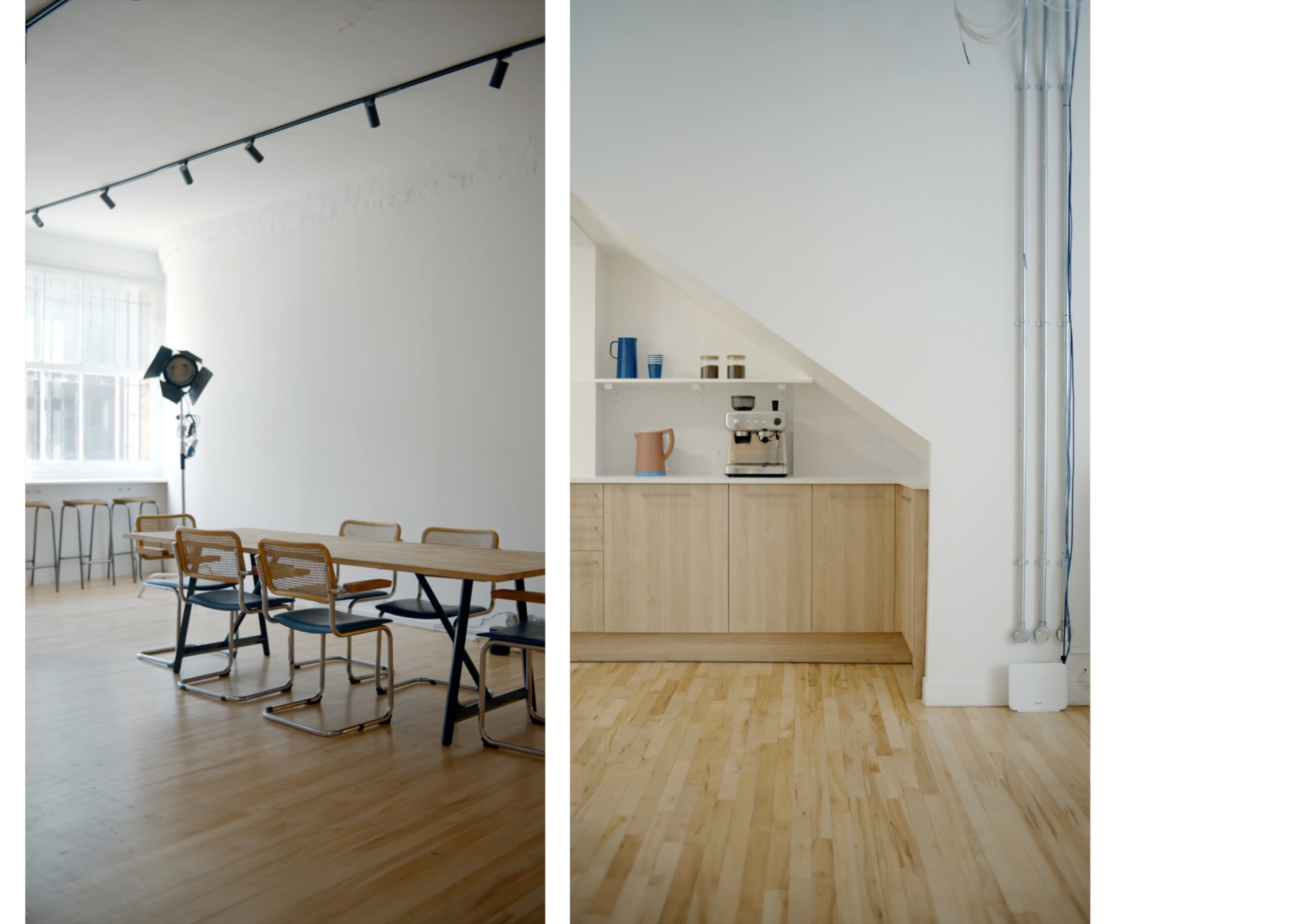 A minimalistic room with wooden flooring, featuring a dining area with several chairs and tables on one side, and a kitchen area with a coffee machine and wooden cabinets on the other side.