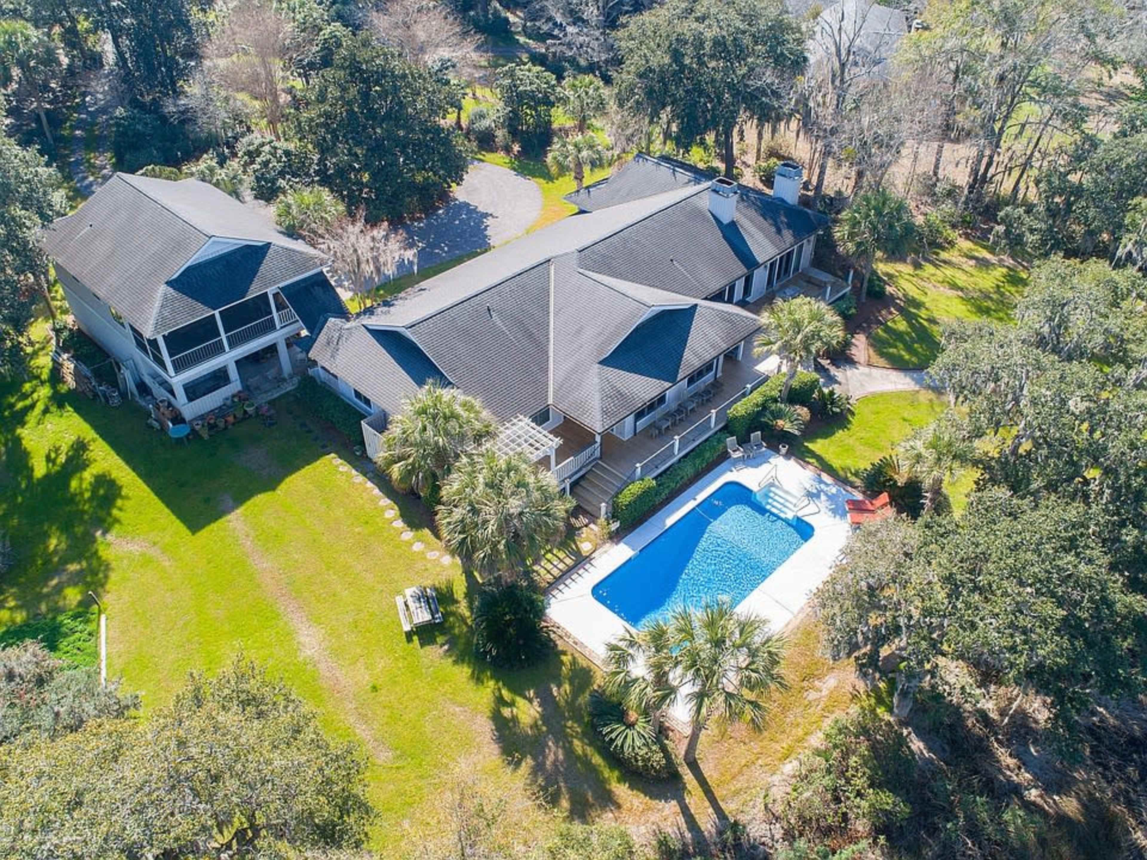 The image shows a large, two-story house with a swimming pool surrounded by greenery and trees.
