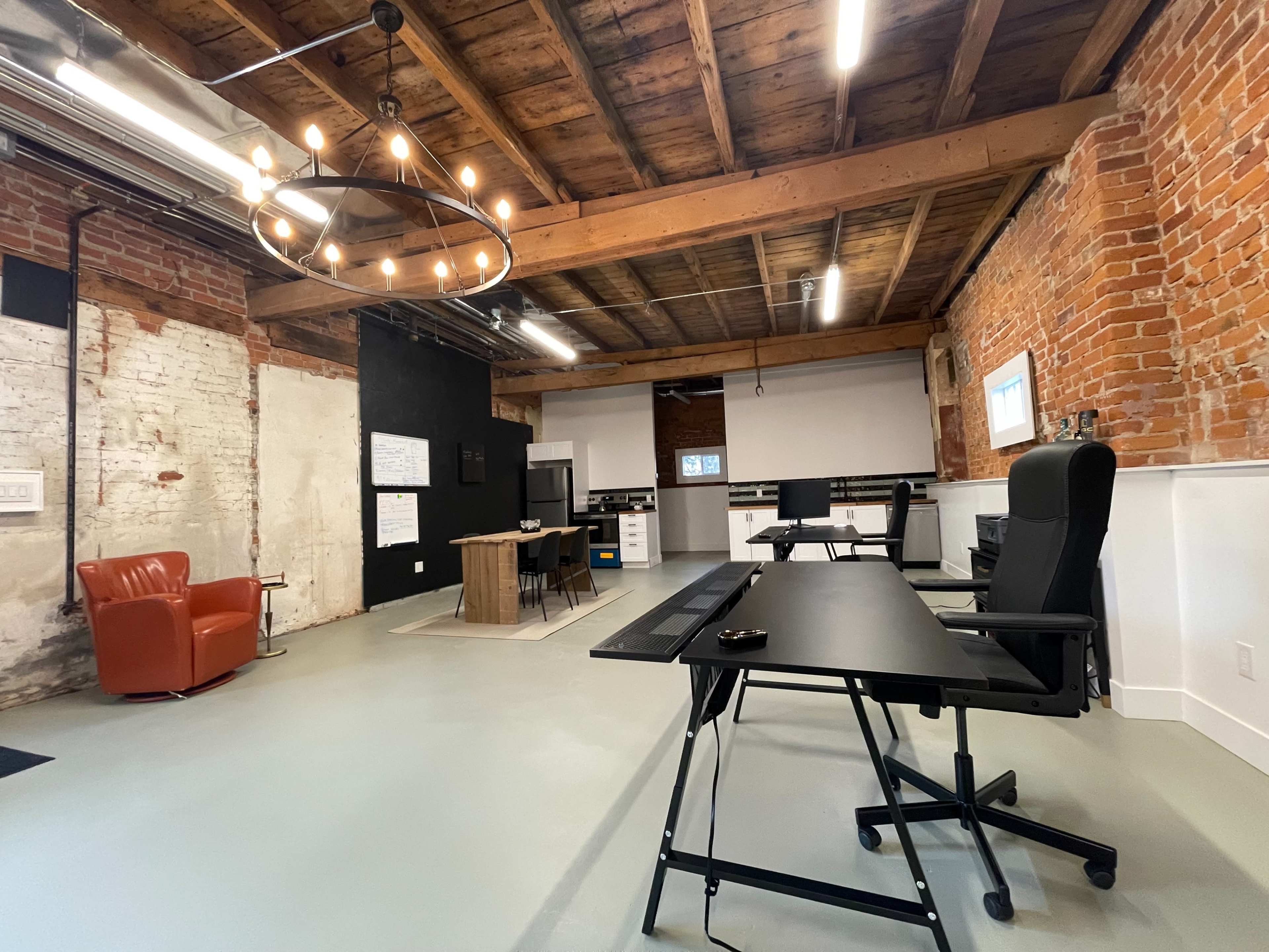 A spacious office with exposed brick walls, wooden beams, and modern furniture, including desks and a lounge chair.