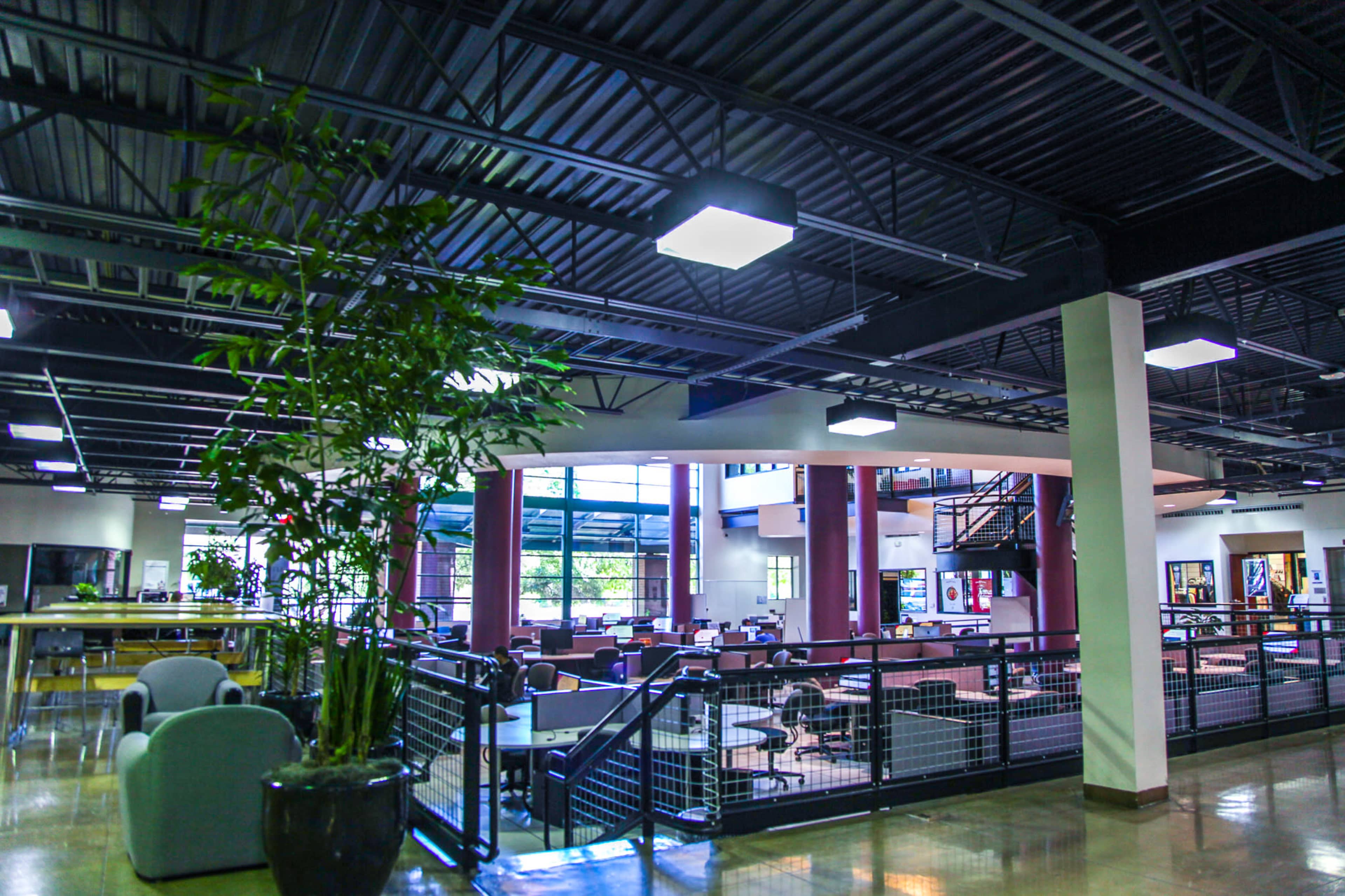 A spacious, modern indoor space featuring seating areas, a staircase, and large windows allowing natural light to enter.